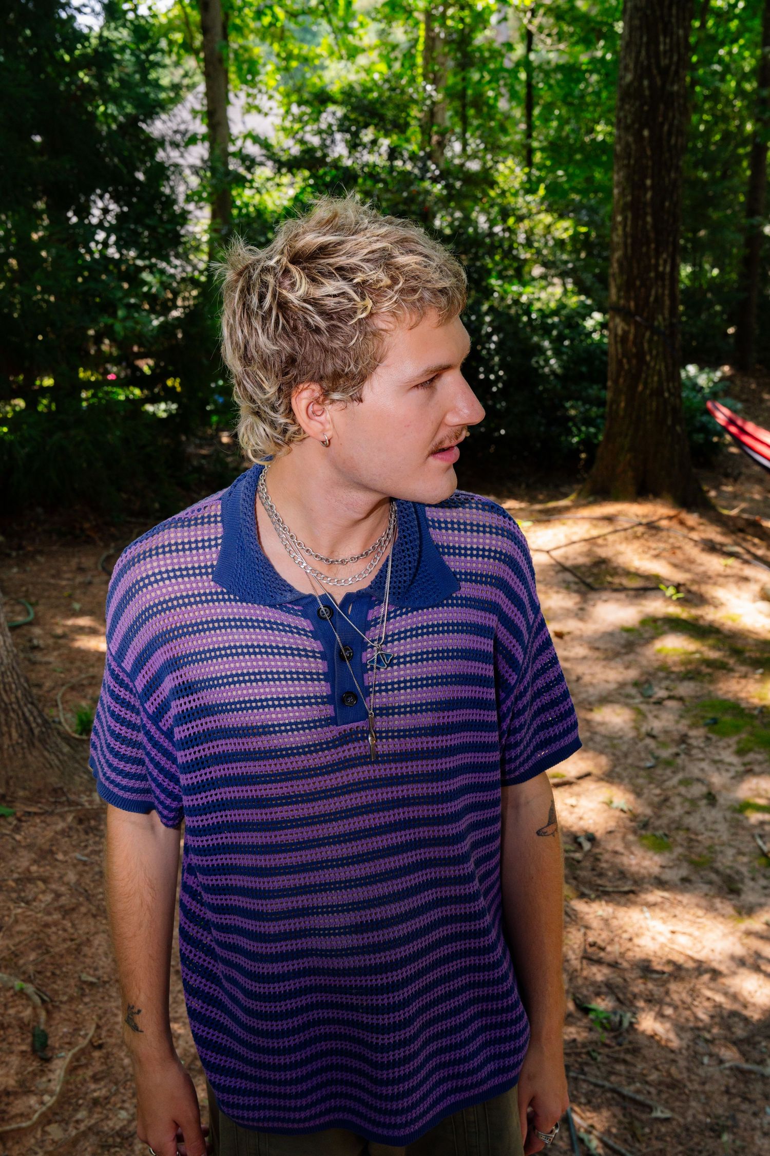 Candid outdoor shot of person in navy striped polo shirt among trees.