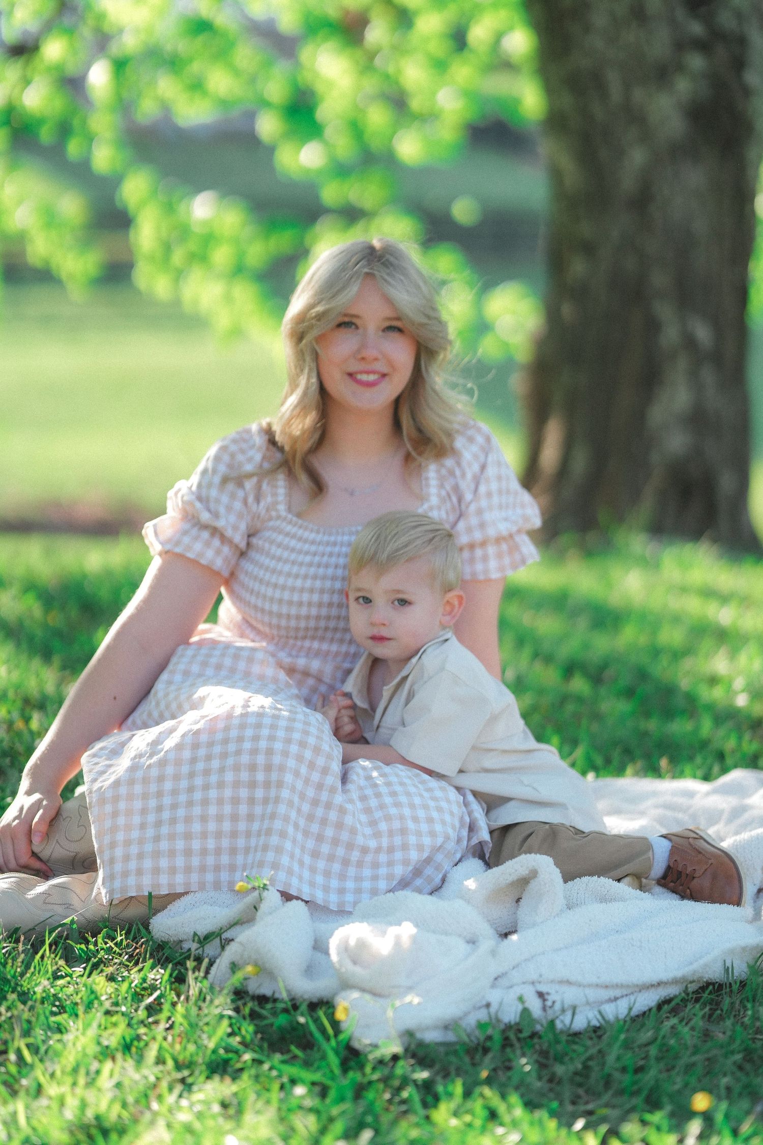 Sweet outdoor portrait session on a white blanket under green trees.