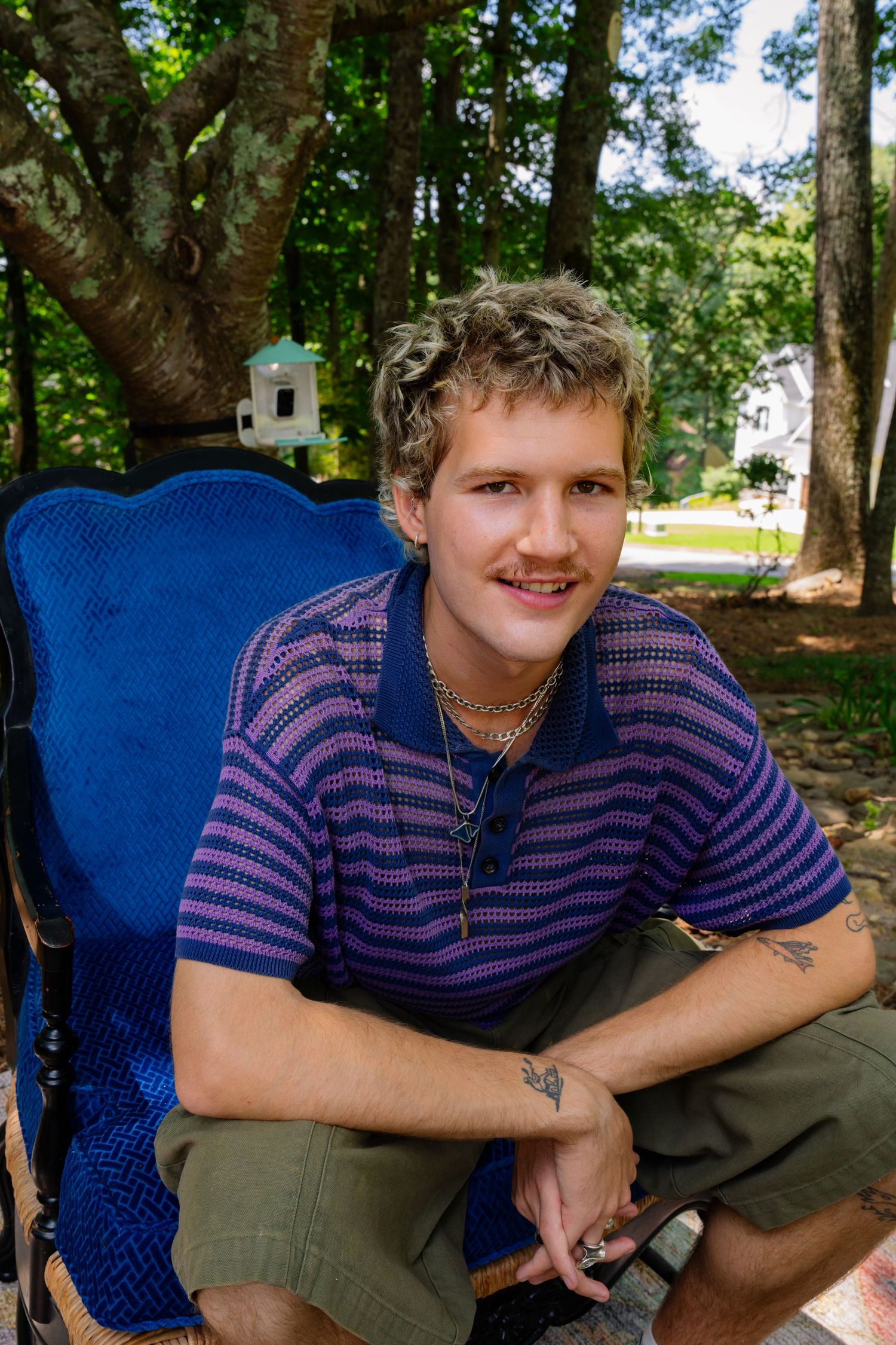 Person in striped shirt and olive pants relaxing in blue chair on patterned outdoor rug.
