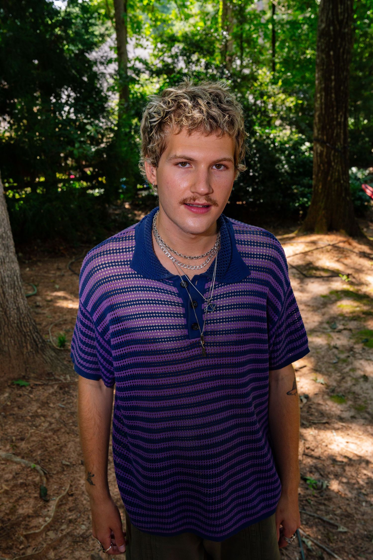Natural outdoor portrait in striped polo with sunlit forest background.