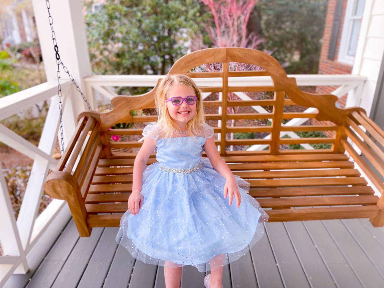 Child in blue tulle dress twirls on wooden porch swing.