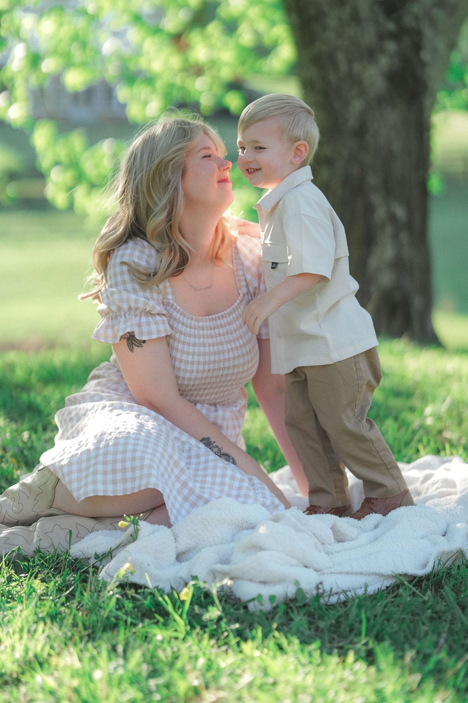 Candid family photos show playful interactions on blanket under shady trees.
