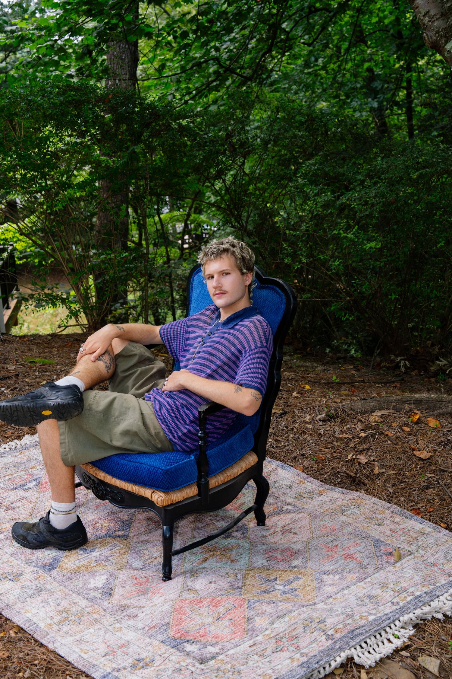 Someone relaxing in a blue outdoor chair set on decorative rug among trees.