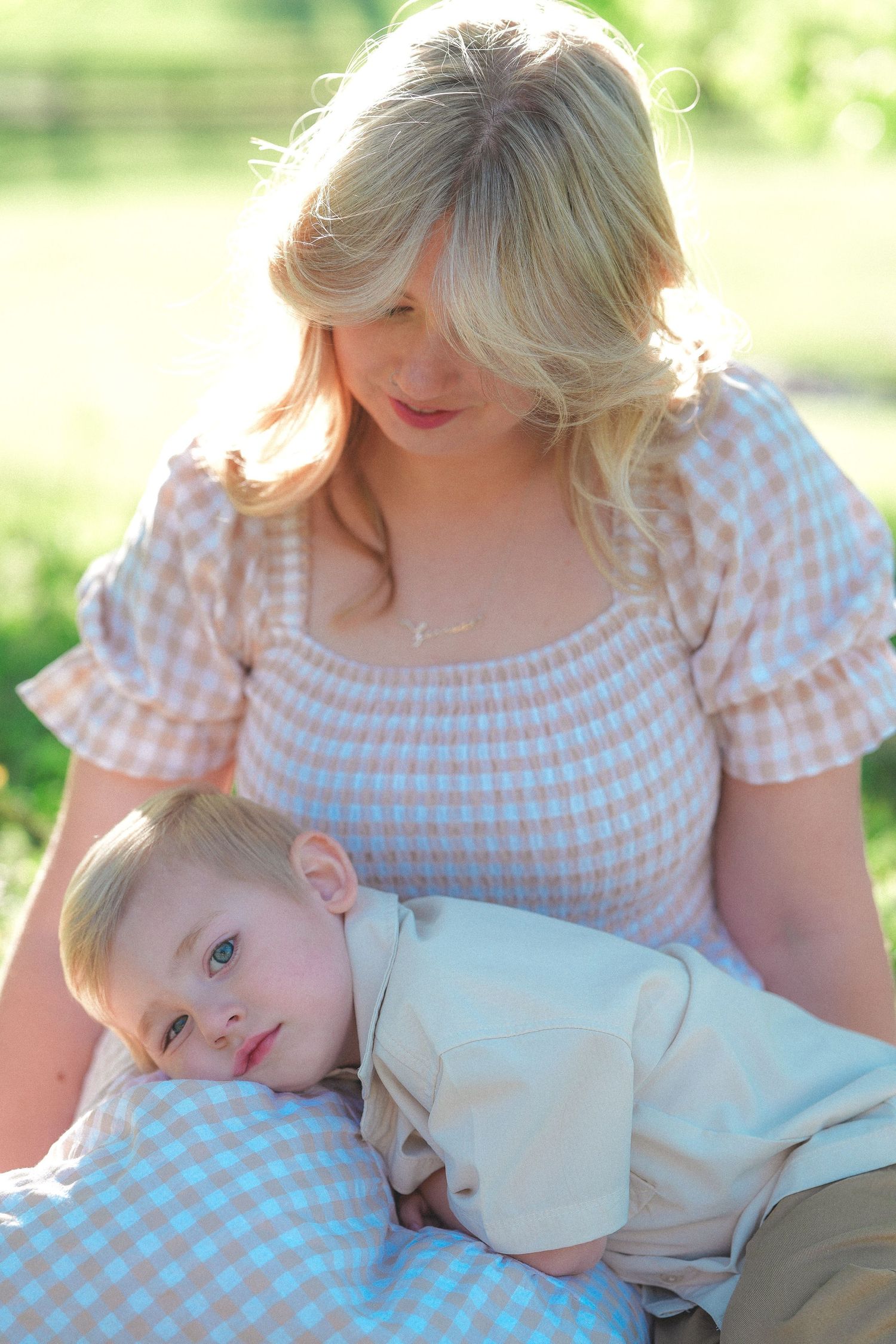 Sweet outdoor moment with gingham dress and white shirt on blanket under sunlit trees.