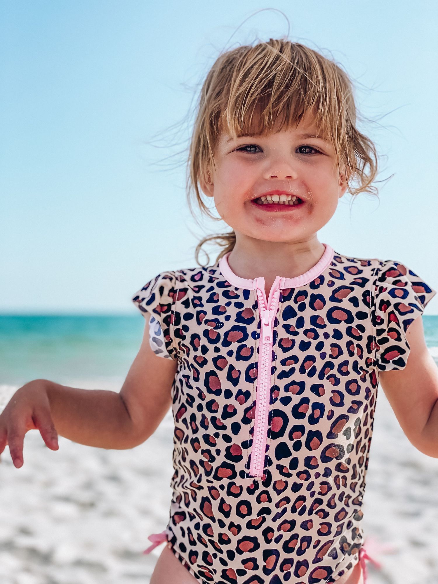 Child in pink leopard print swimsuit plays on sunny beach.