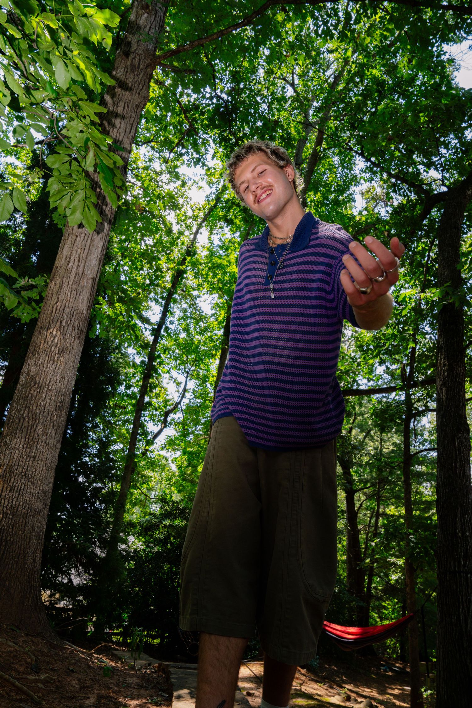 A candid outdoor scene with someone in a striped purple polo shirt against a leafy green forest background.