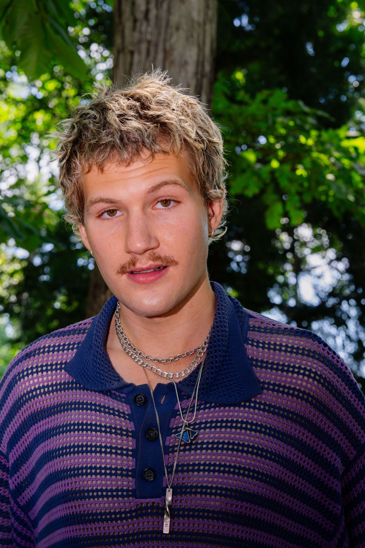 Close-up outdoor portrait showing striped polo and silver chain necklace.
