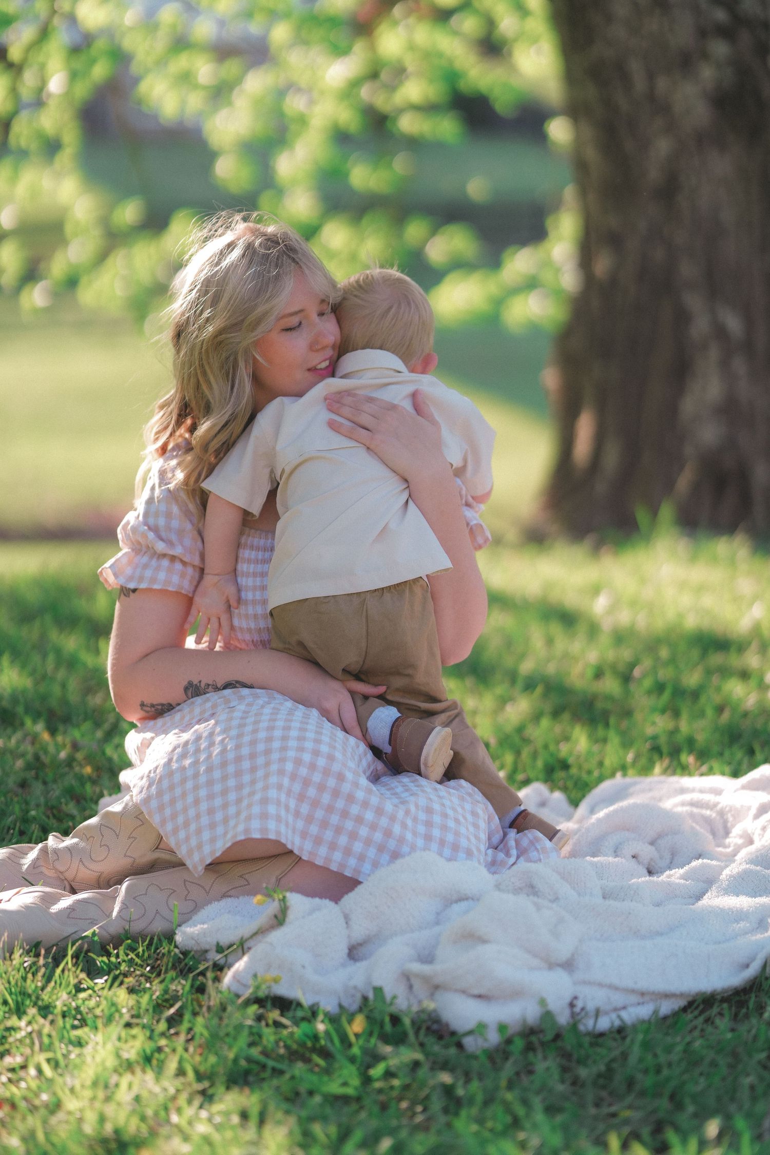 Tender moment shared on a white blanket under trees in a sunlit park.