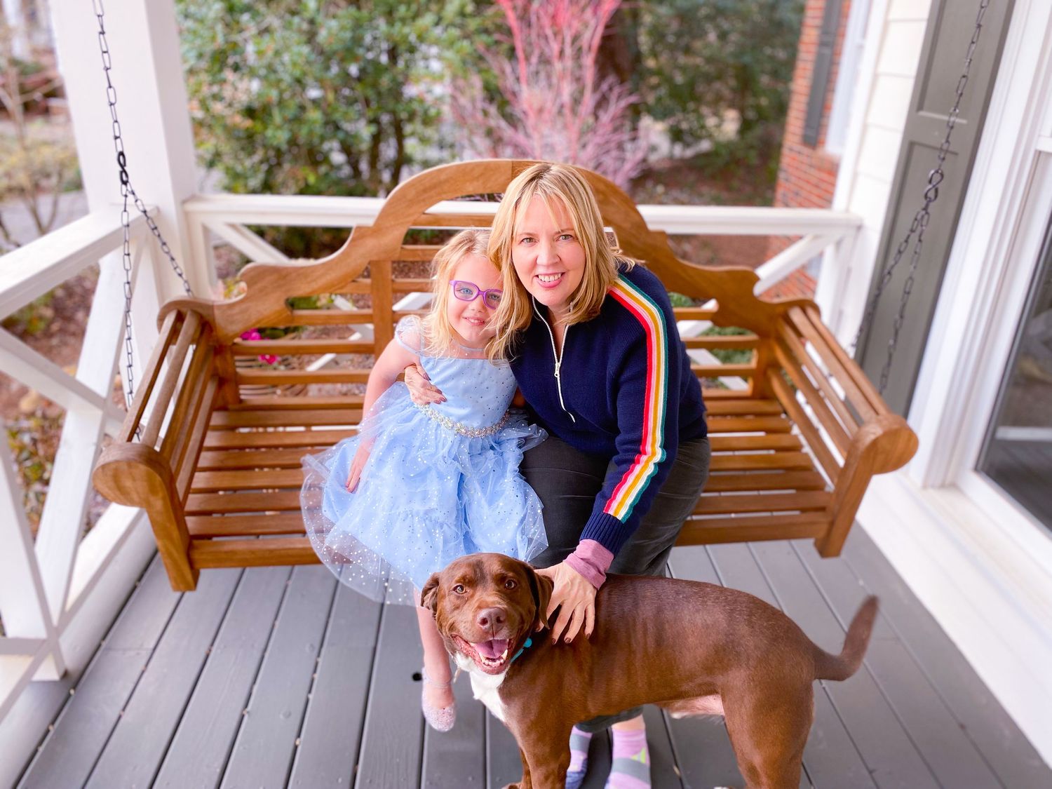Porch scene with wooden swing, dog, and people enjoying outdoor setting.