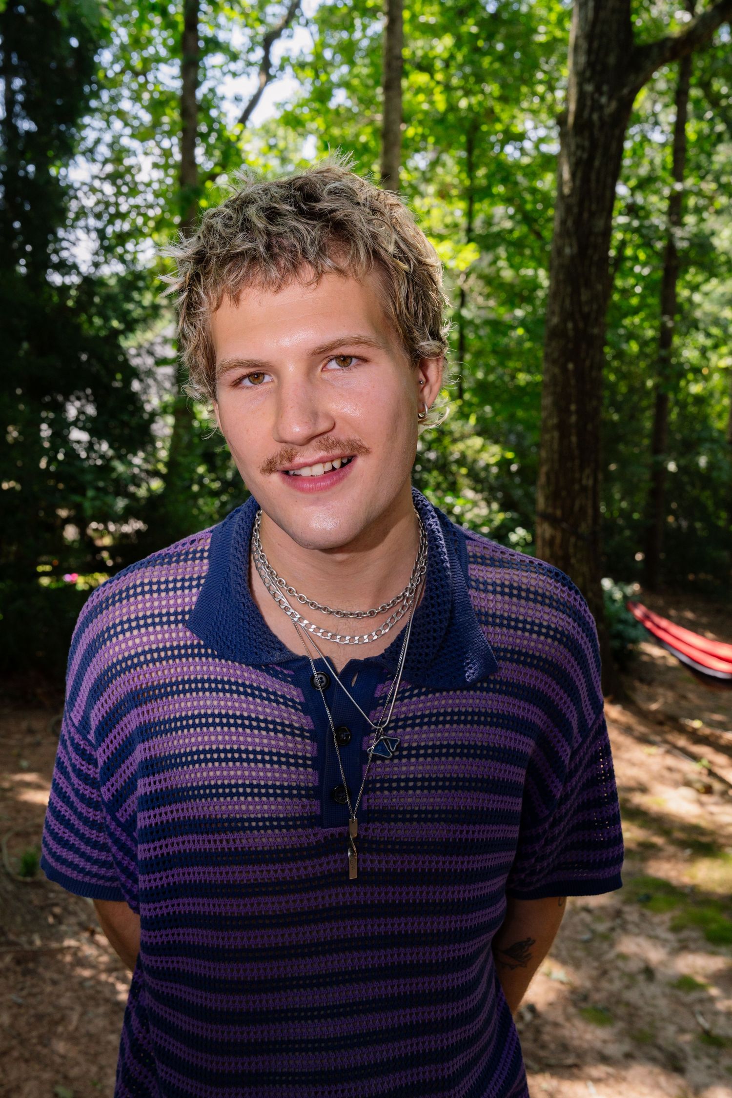 Smiling outdoor headshot with striped polo and natural forest lighting.