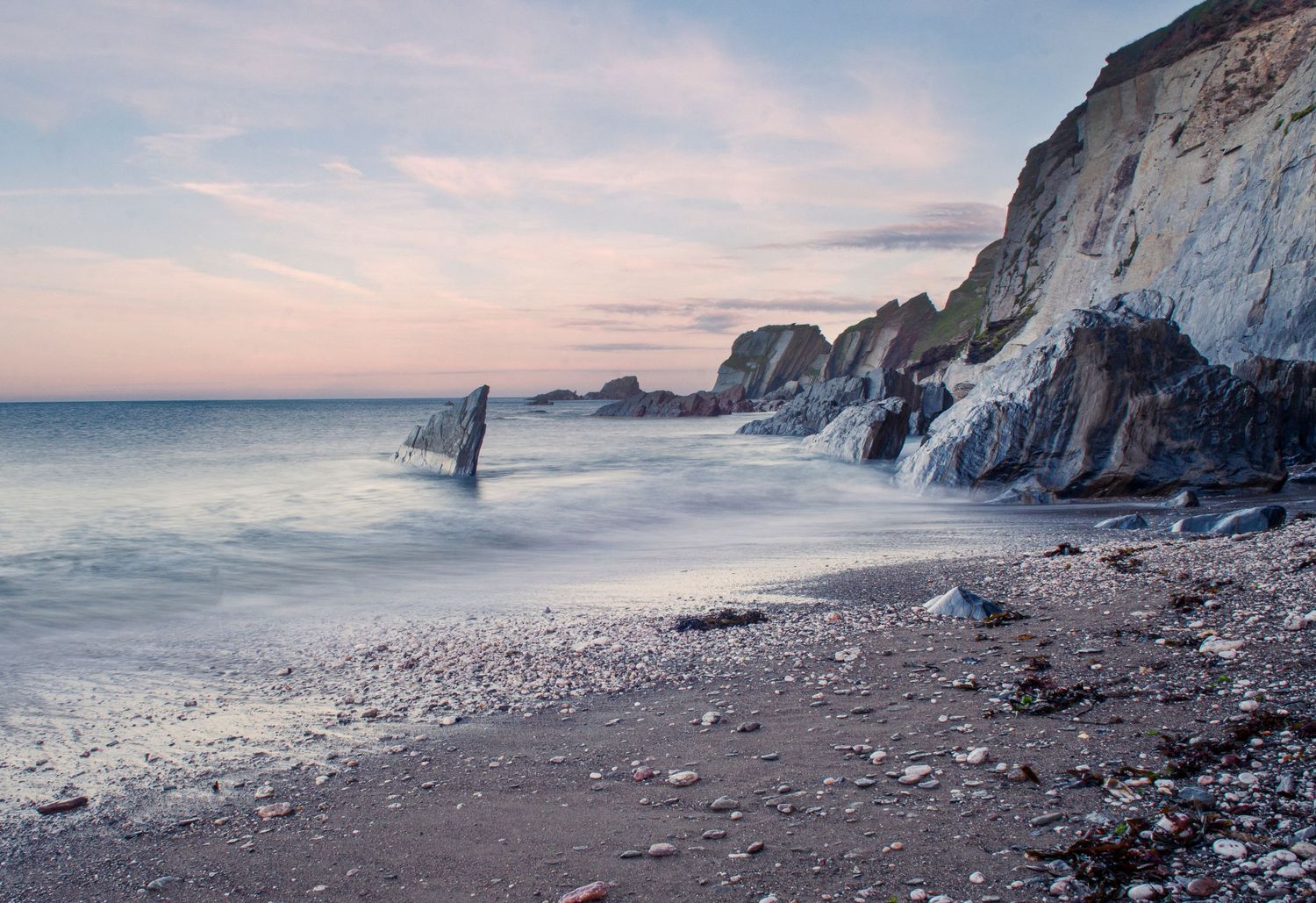 Dramatic coastal landscape with white chalk cliffs along a rocky beach during sunset with calm ocean waters.