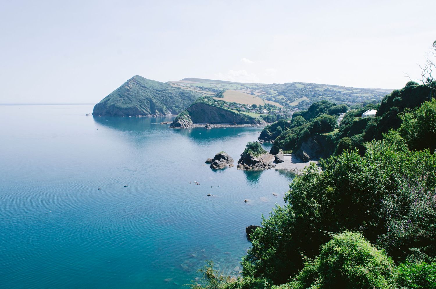 Dramatic coastal cliffs overlooking turquoise waters with lush green vegetation along the rugged shoreline of North Devon