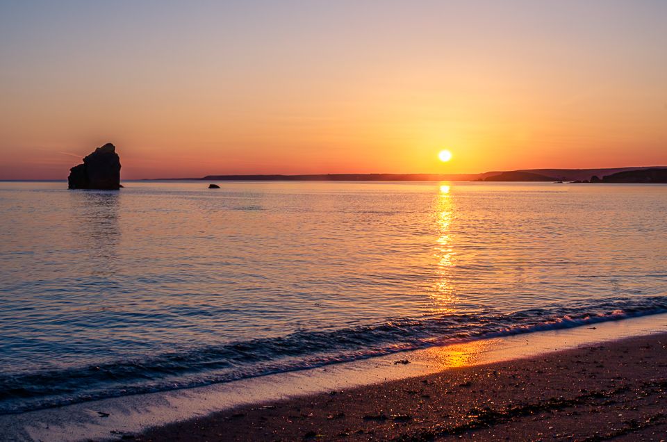 A picturesque sunset over a calm ocean with golden light reflecting on the water's surface creating a serene coastal view.