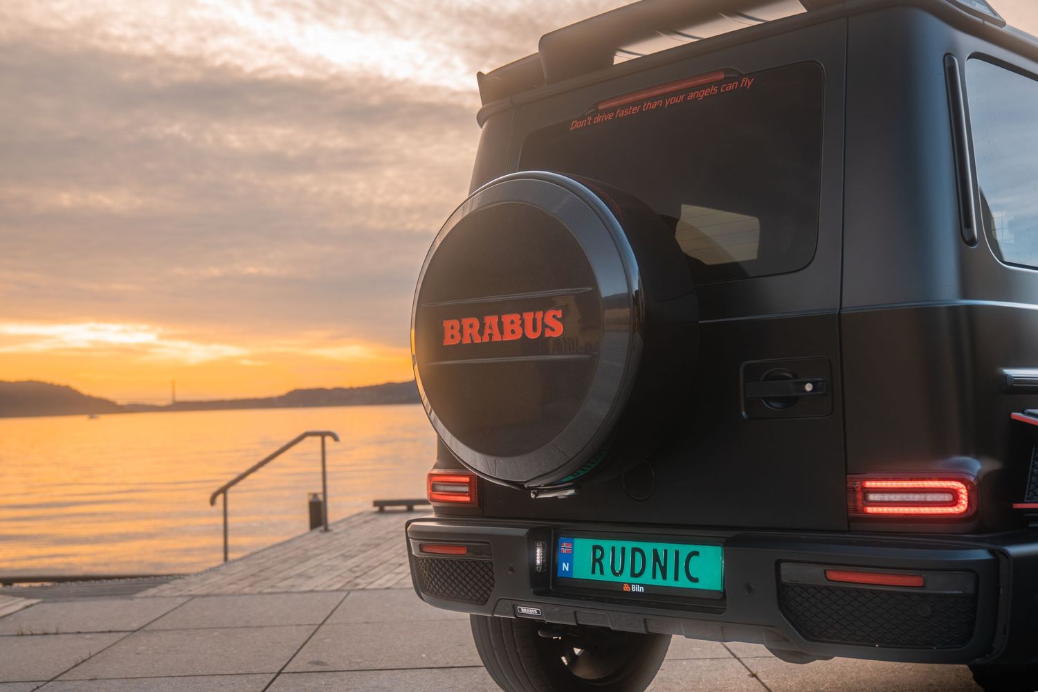 Luxury black Mercedes G-Wagon Brabus with custom wheels parked at sunset against an orange sky backdrop.