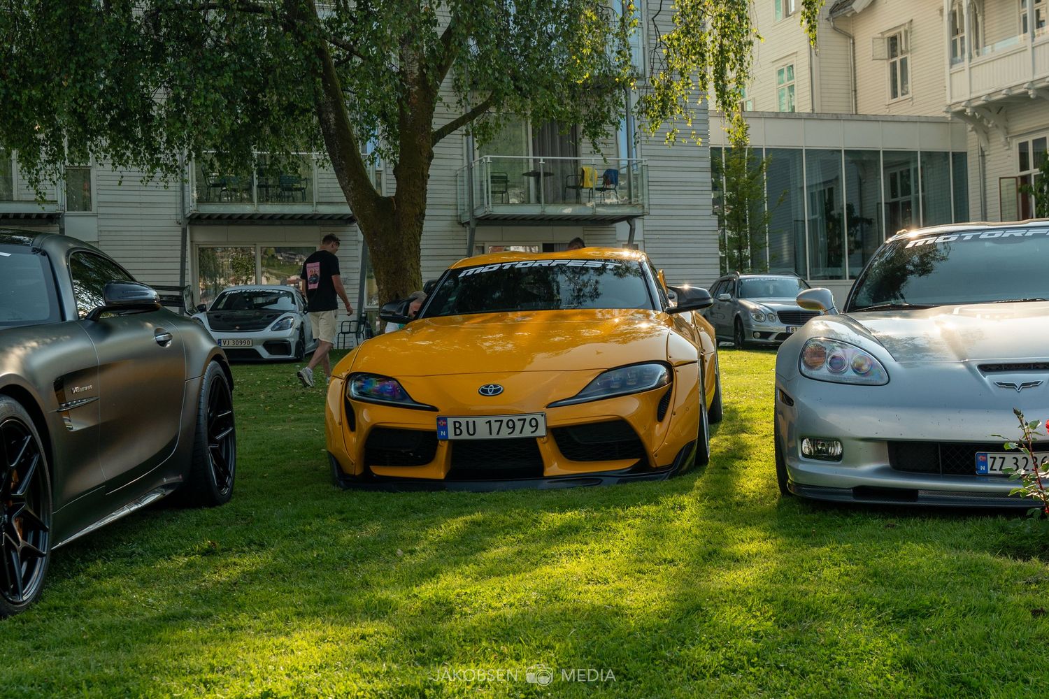 Collection of exotic sports cars including McLaren and Lamborghini models lined up on grass near buildings.