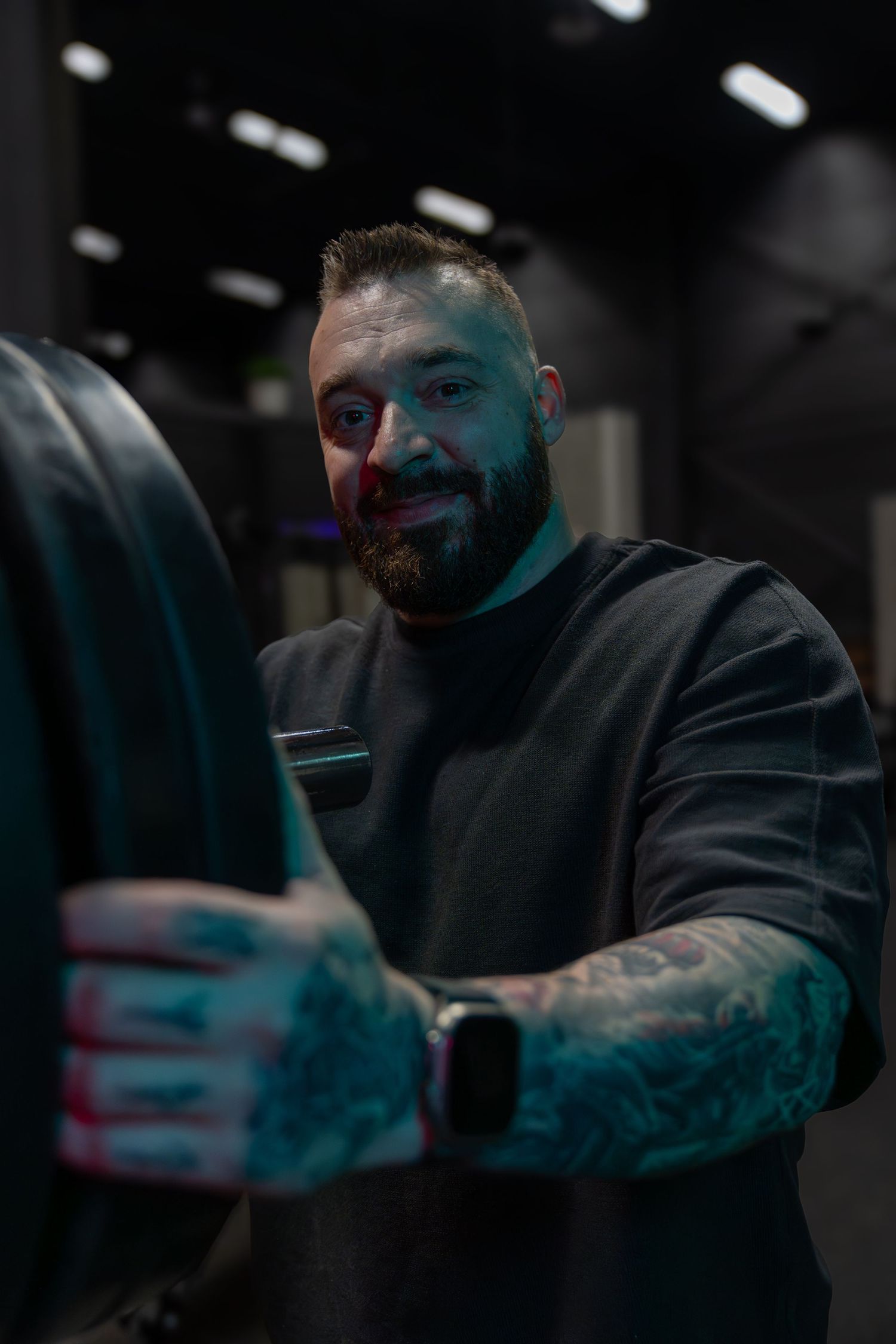 Person in dark gym setting handling fitness equipment with colorful ambient lighting.