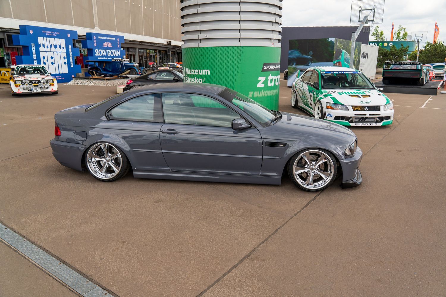 Modified gray BMW M3 with aggressive stance and custom wheels parked at a motorsport event.