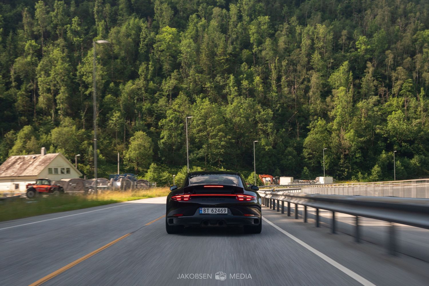 Black sports car driving on mountain road with scenic forest backdrop.
