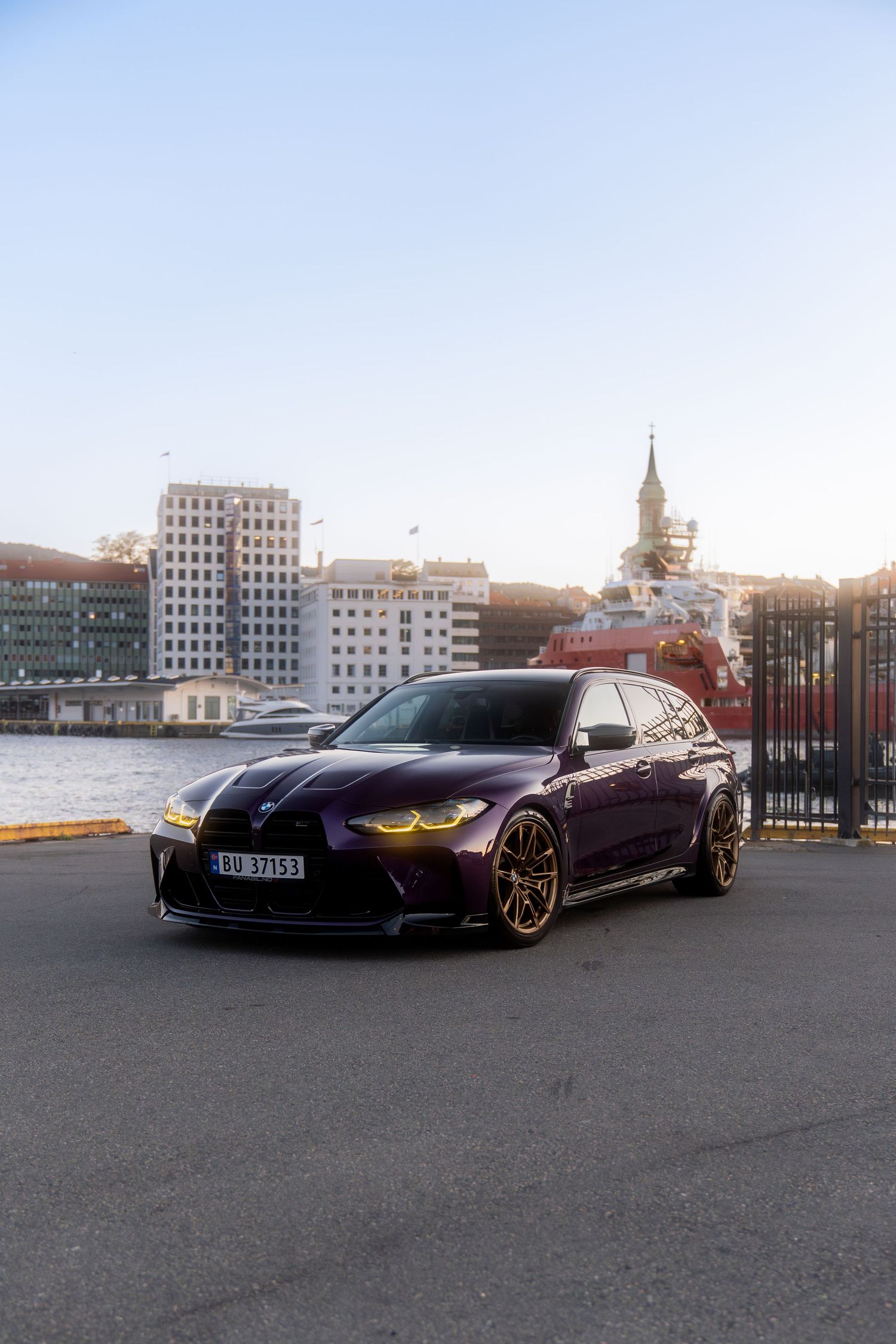 Purple luxury sports car parked with waterfront buildings visible in the background.