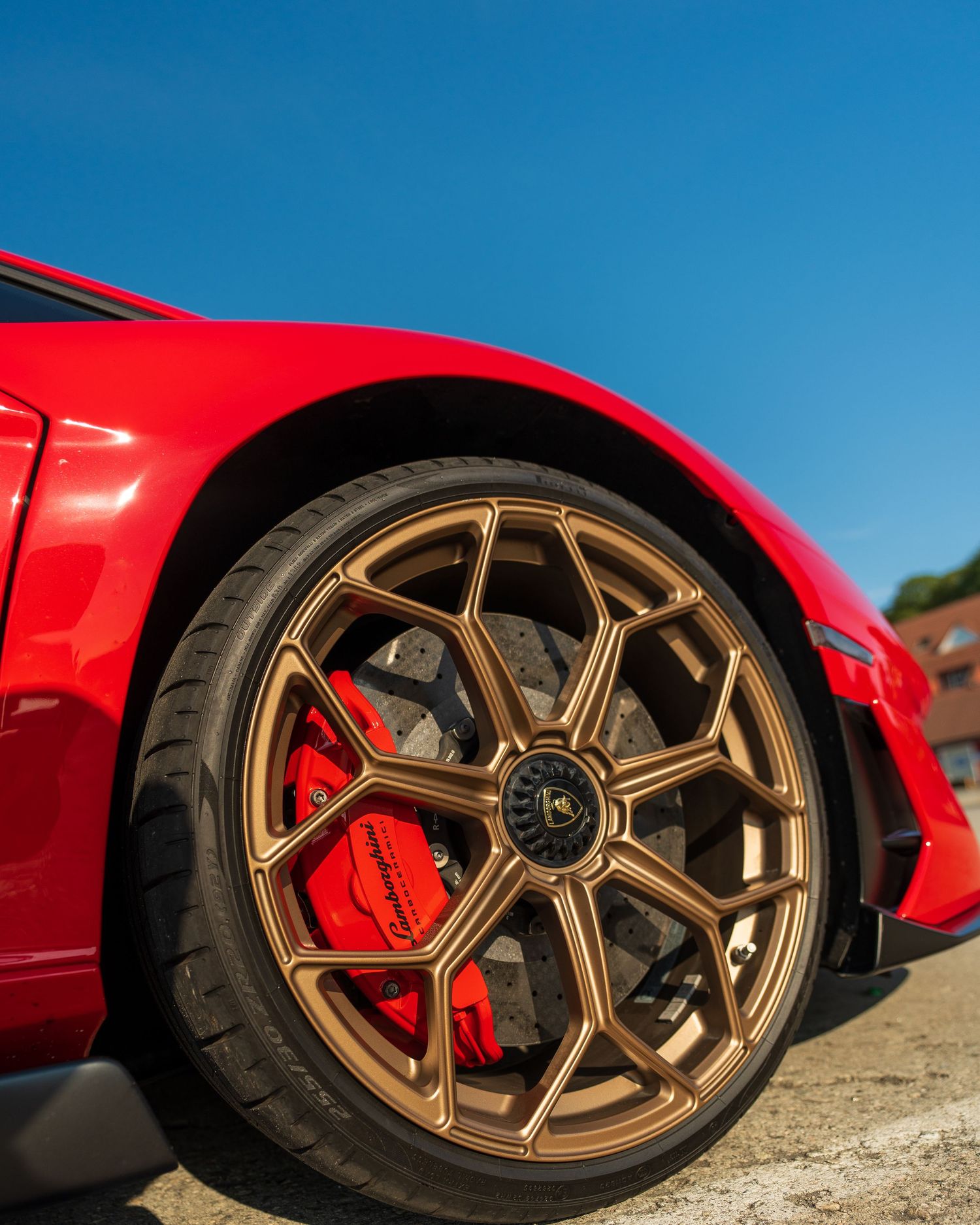Close-up of a red sports car's bronze wheel and red brake caliper against a bright blue sky.