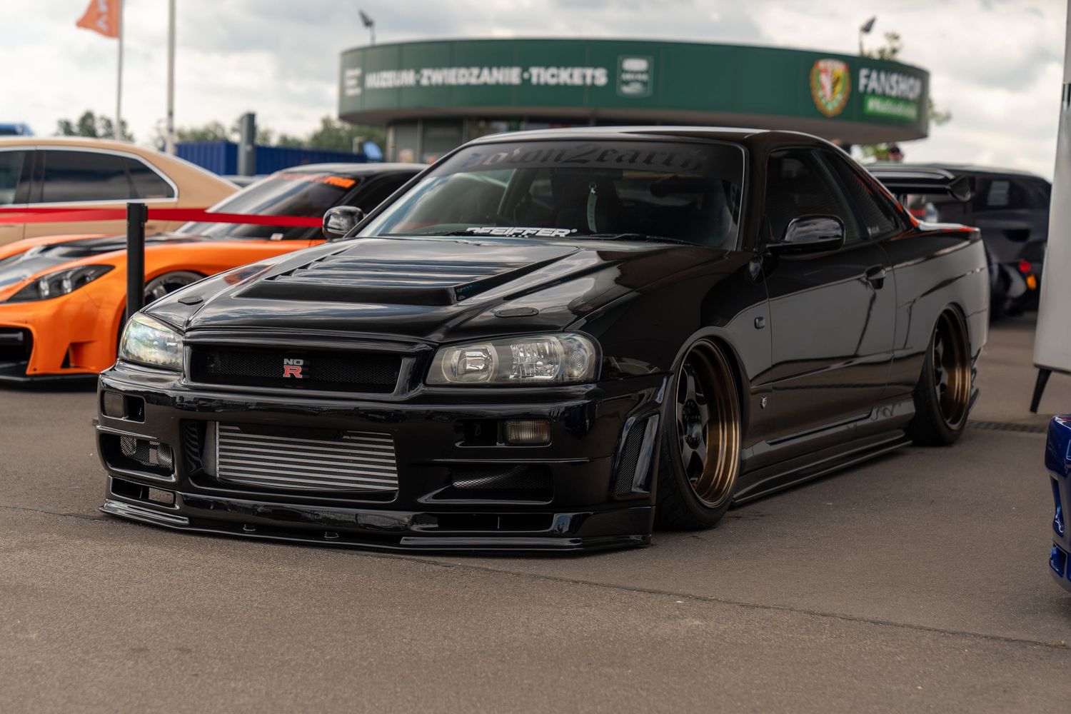 Collection of modified JDM cars including black Nissan Skylines with aggressive stance.