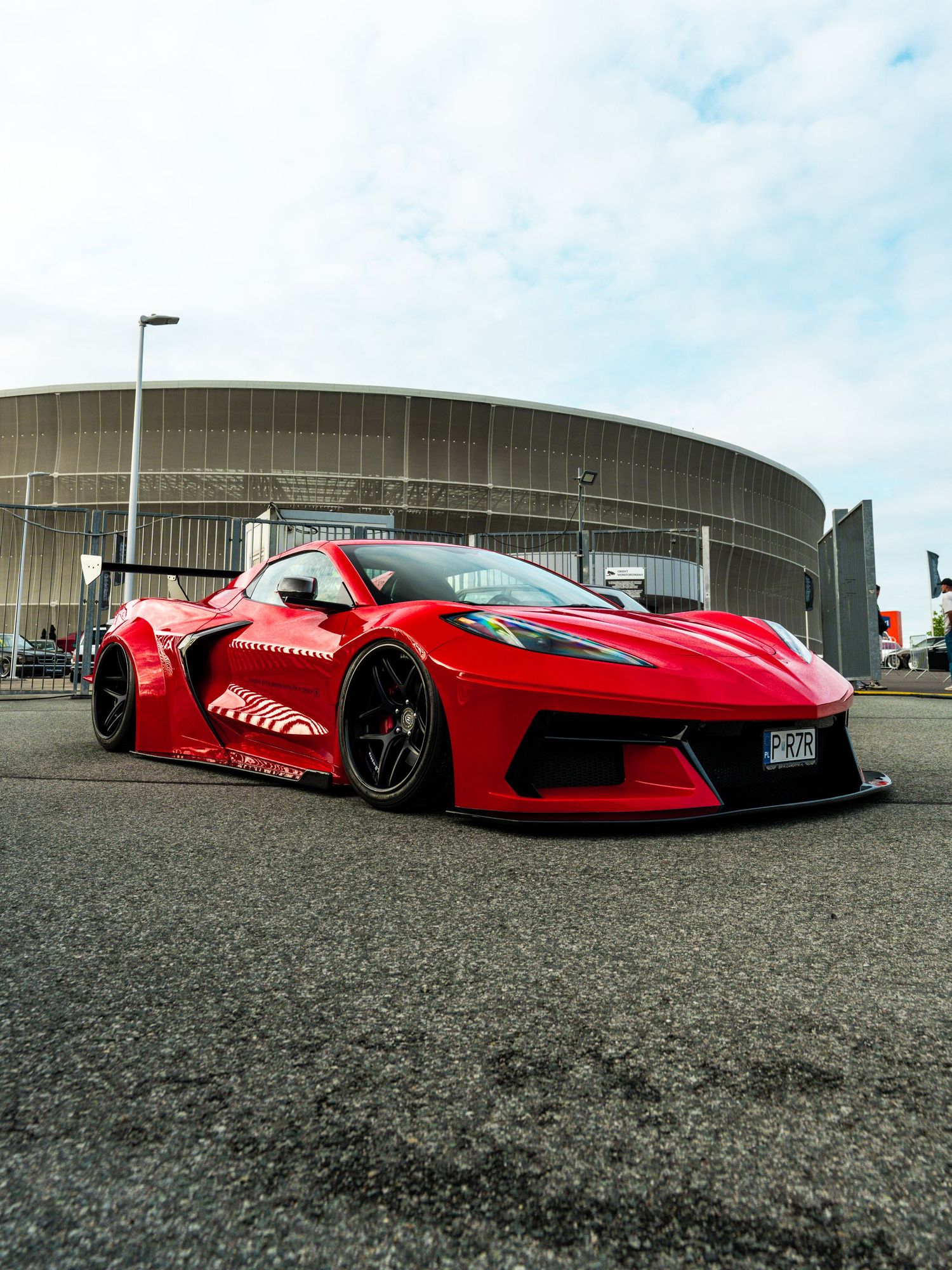Bright red modified Chevrolet Corvette C8 parked in front of a curved building with tinted windows.