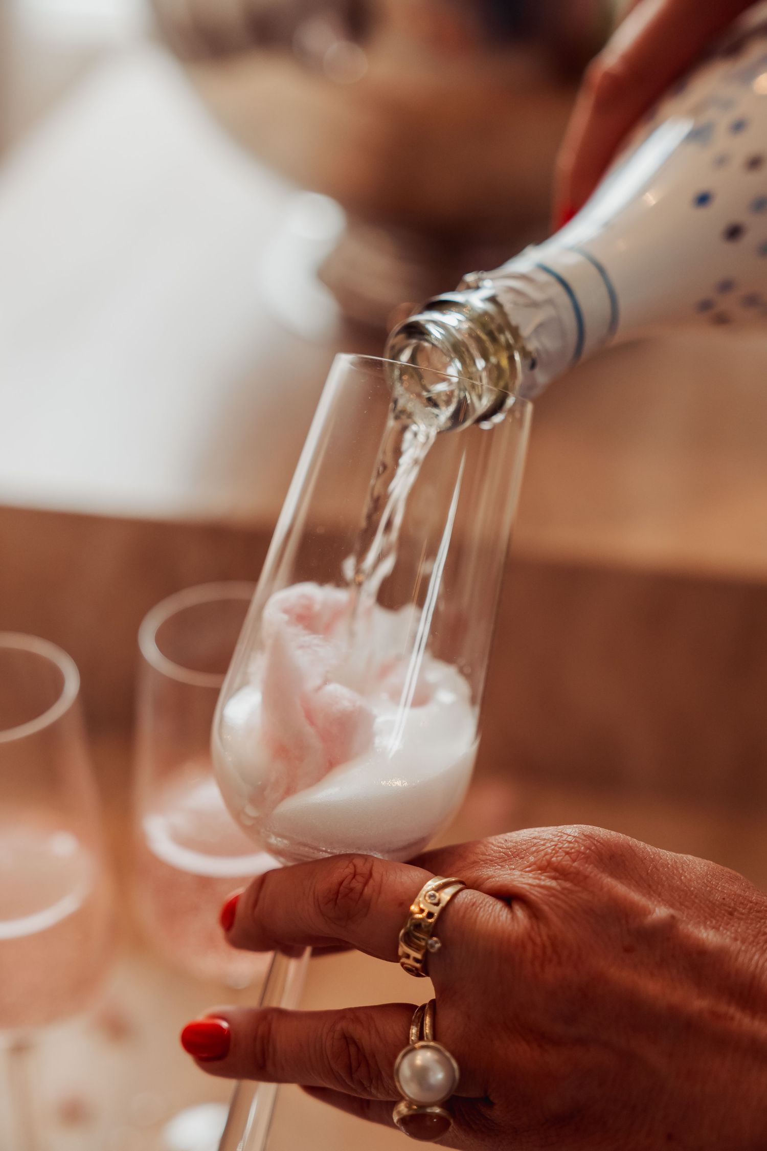 Pouring sparkling wine into glass with decorated hand wearing rings in warm lighting.