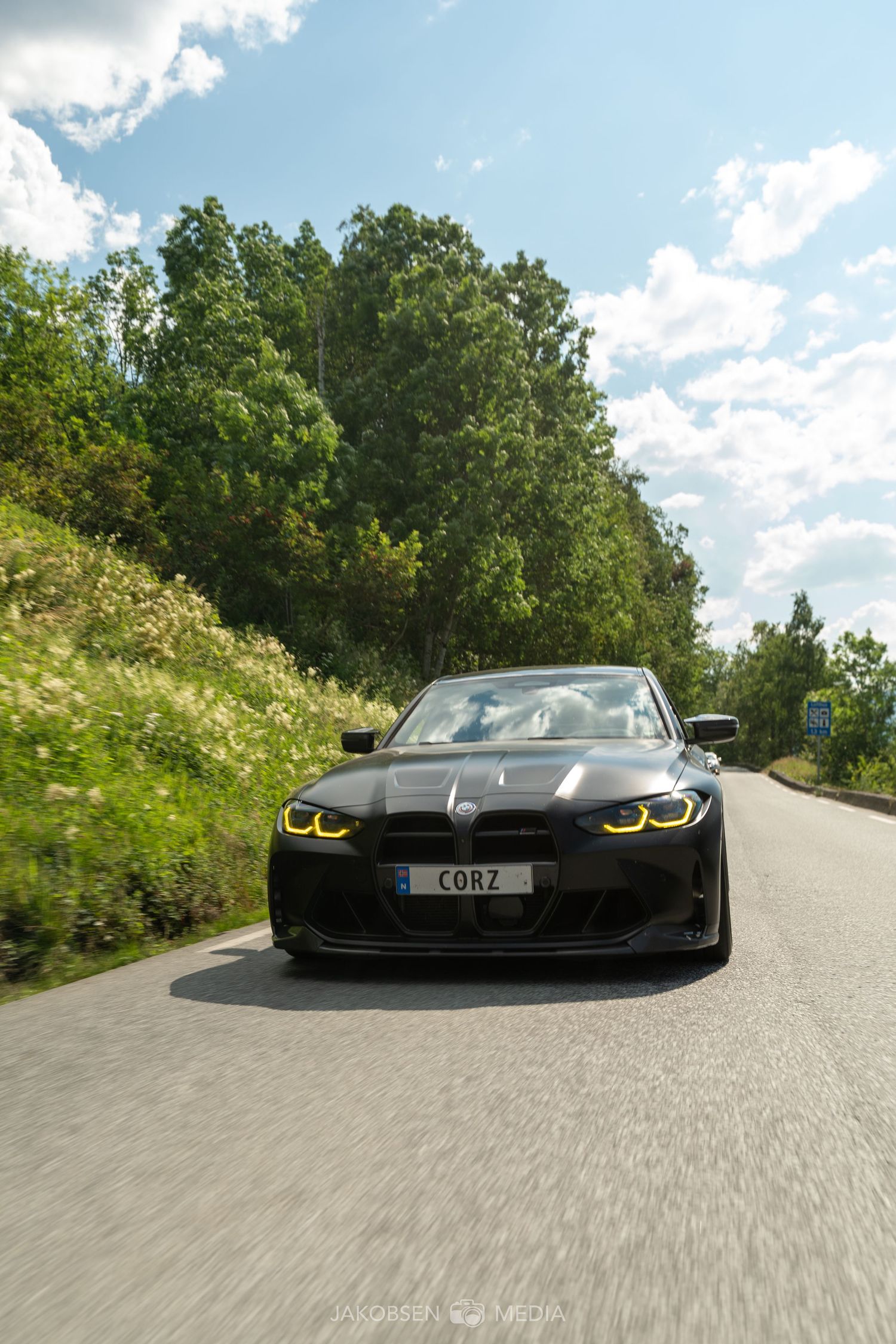 Black BMW M4 sports car photographed from a low angle on a curving mountain road.