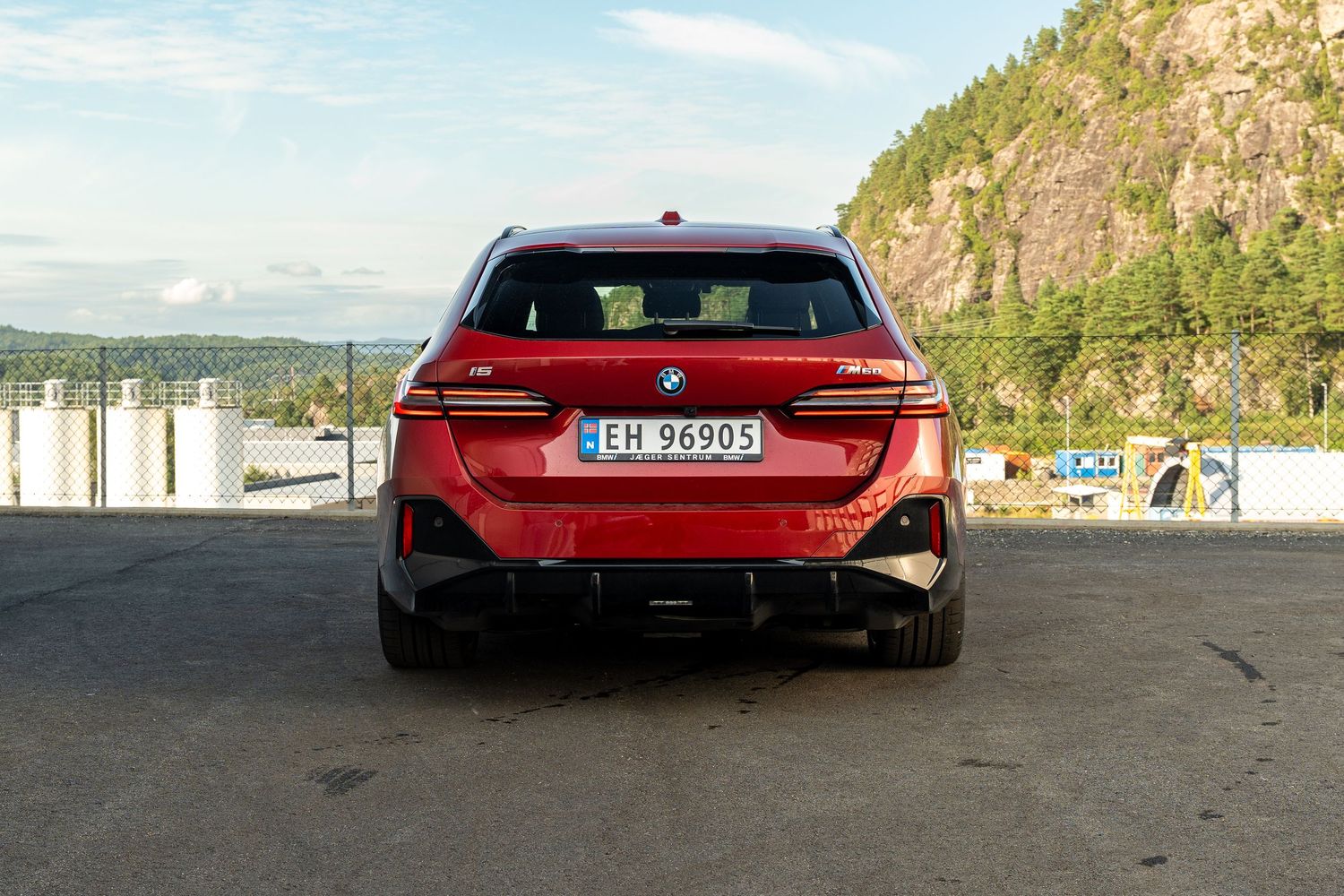 A red BMW M5 CS sports sedan parked in a mountainous coastal setting showcasing its dynamic rear design features.