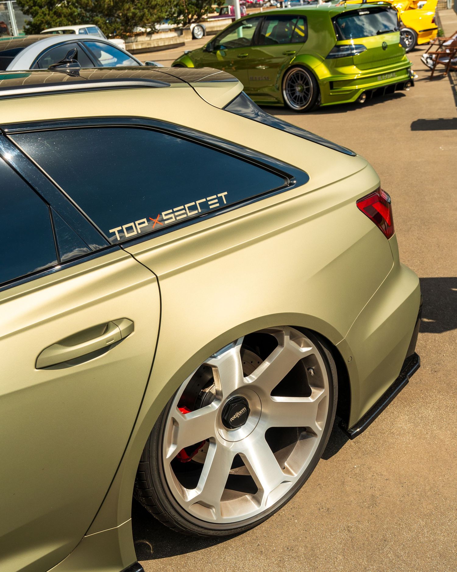 Modified beige car with custom wheels and top secret badging on display at car show.