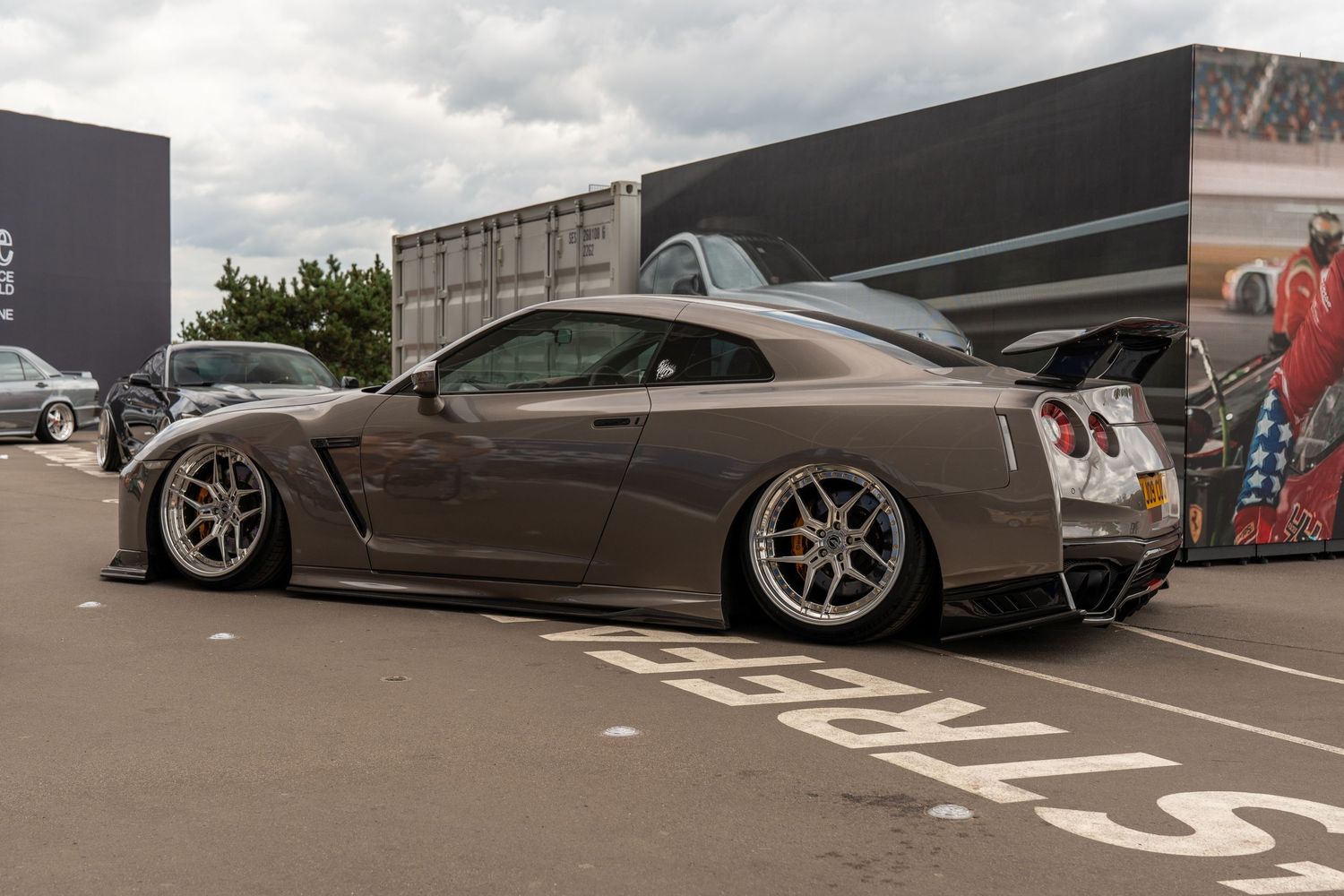 A modified grey Nissan GT-R with aggressive stance and custom wheels parked at a car event.