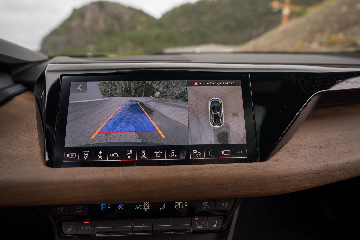 Wide angle car infotainment screen displaying surround view camera system on a mountain road.