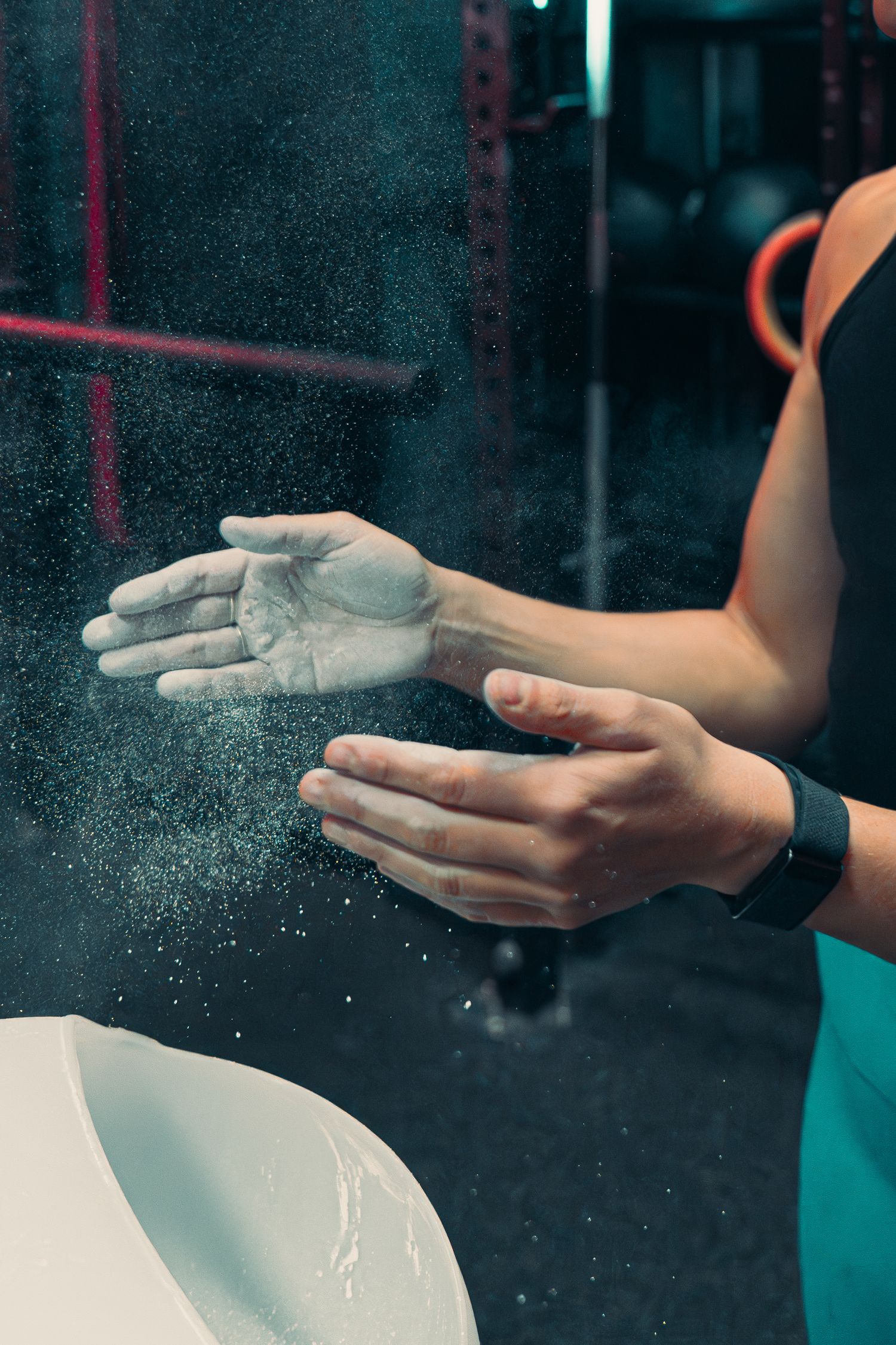 Hands applying chalk powder with dust particles visible in dark gym setting.