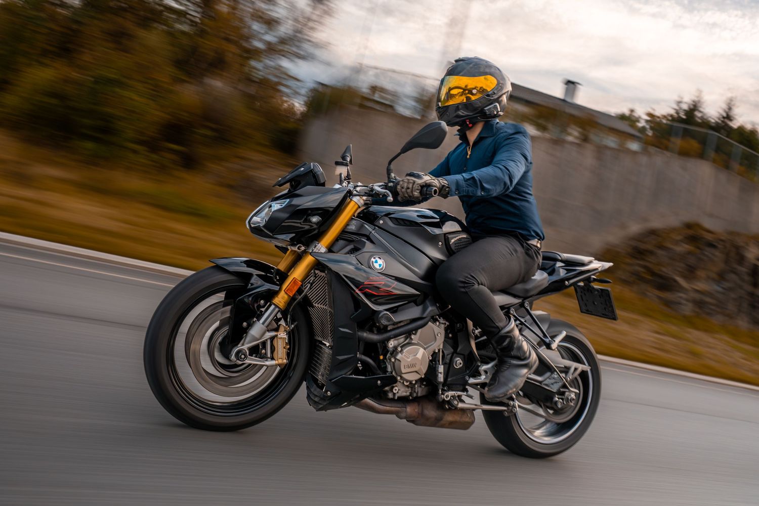 Rider in blue jacket and yellow helmet navigating a black BMW motorcycle on an open road at speed.