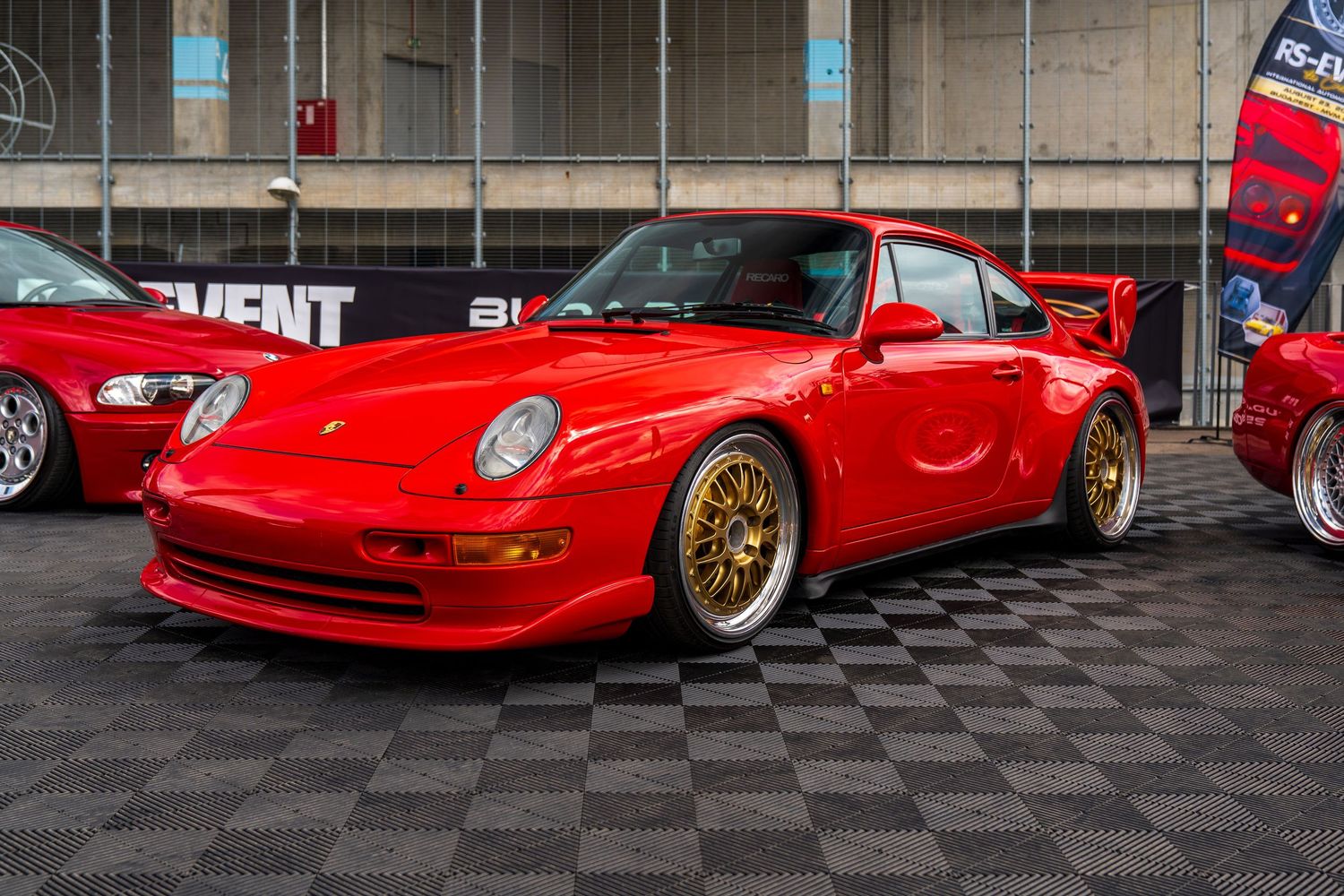 Classic red Ferrari sports cars showcased on checkered flooring at an indoor auto exhibition.