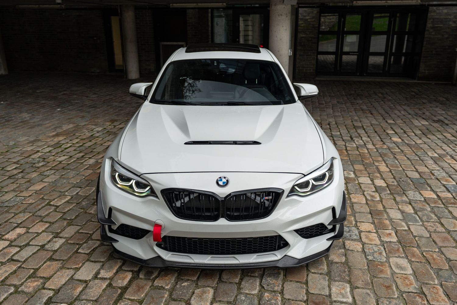 Front view of white BMW M2 Competition showcasing aggressive front splitter and hood design.