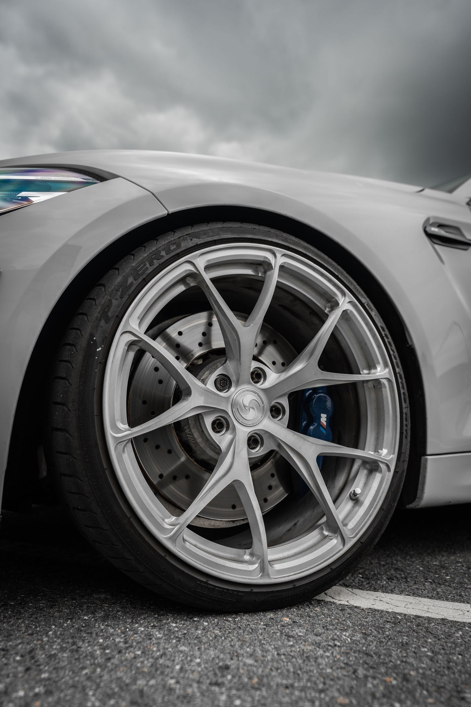 Close-up of a silver sports car wheel with high-performance brake calipers and alloy rim design.