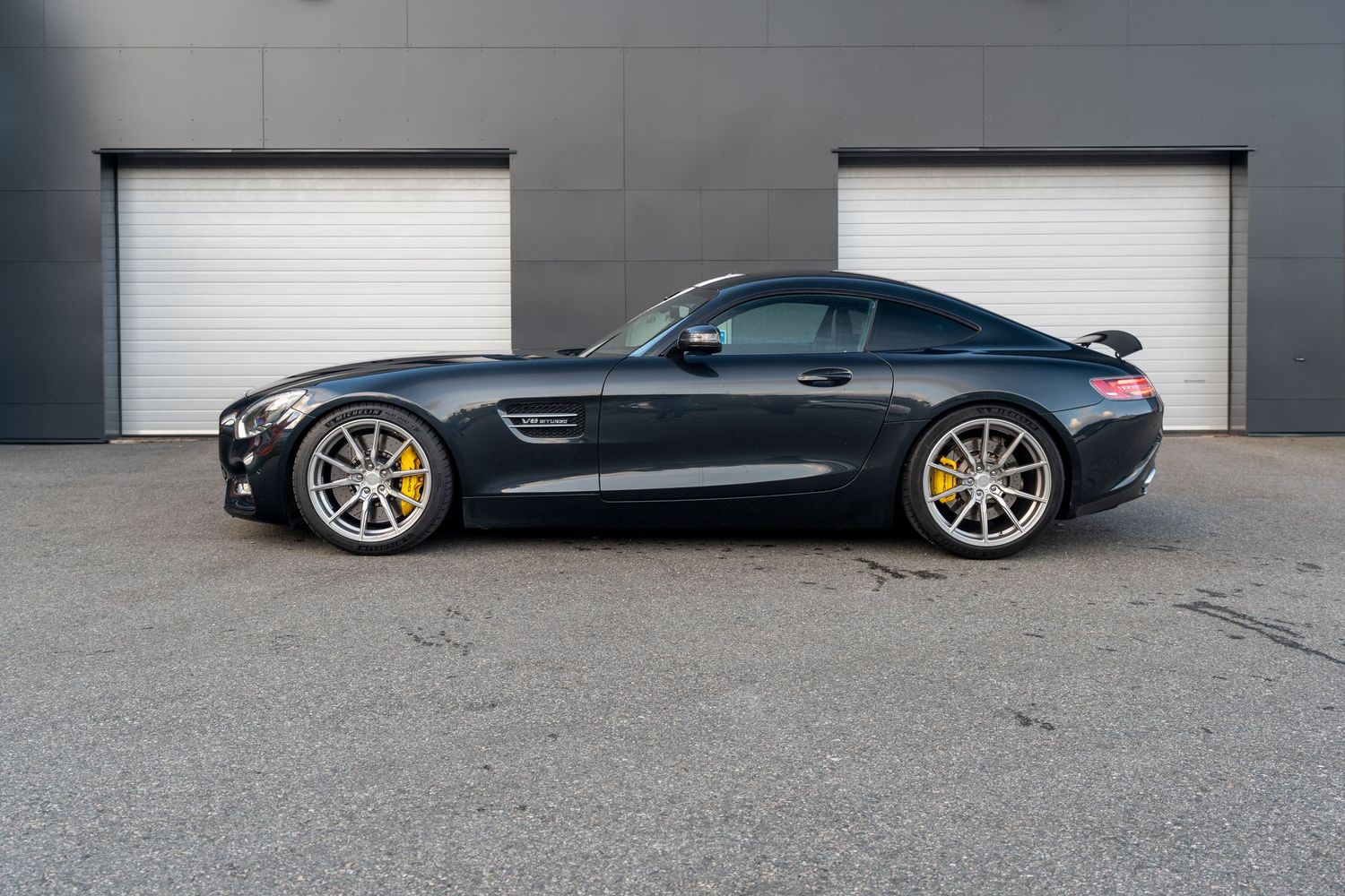 Black Mercedes-AMG GT sports car with gold wheels parked in front of white garage doors.