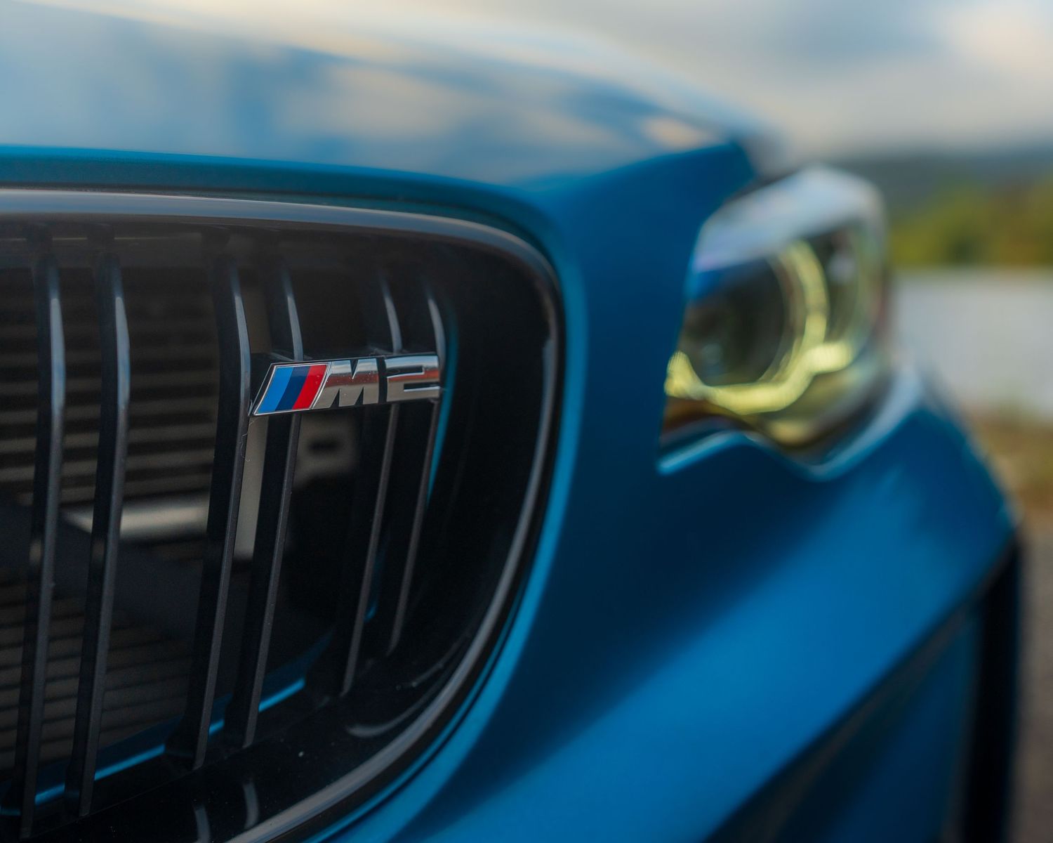Close-up detail shot of a BMW M logo badge and grille on a blue M-series vehicle.