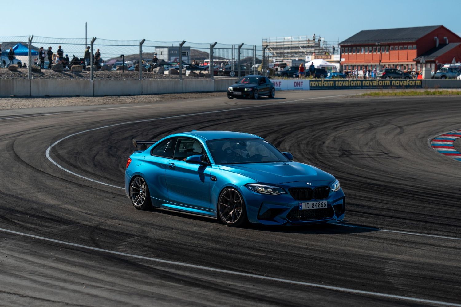 A bright blue BMW M2 drifting on a racetrack curve with tire marks visible on the asphalt.
