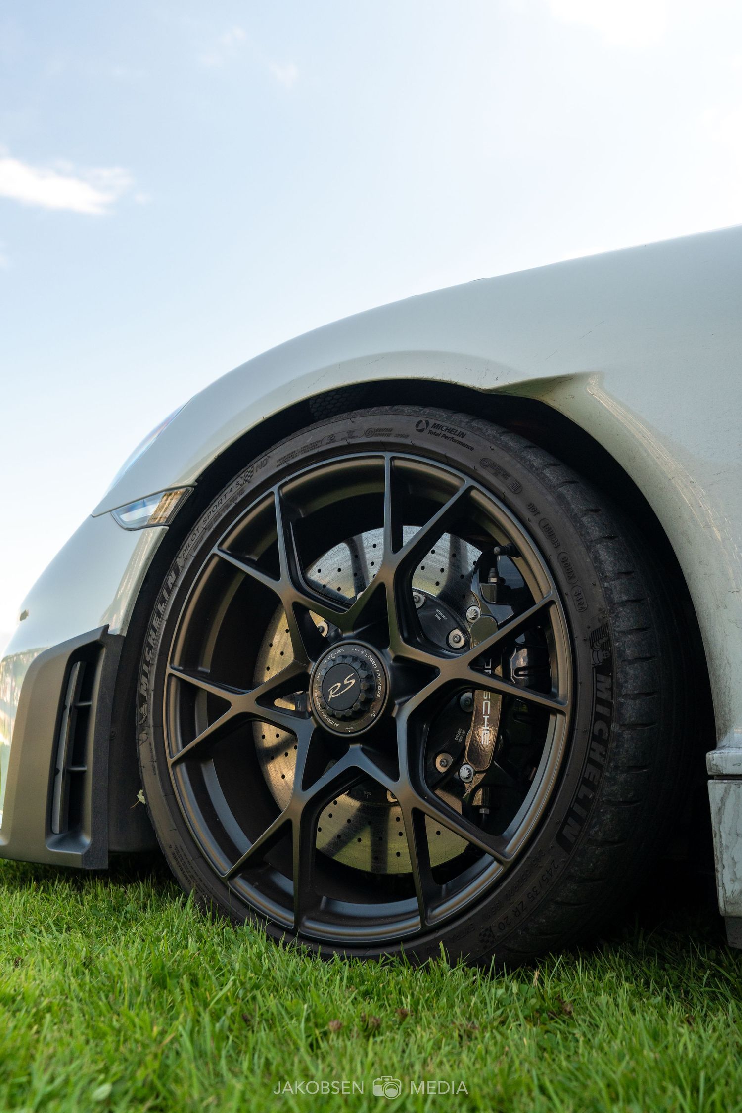 Close-up of black performance wheels and gold brake calipers on white sports car resting on grass.
