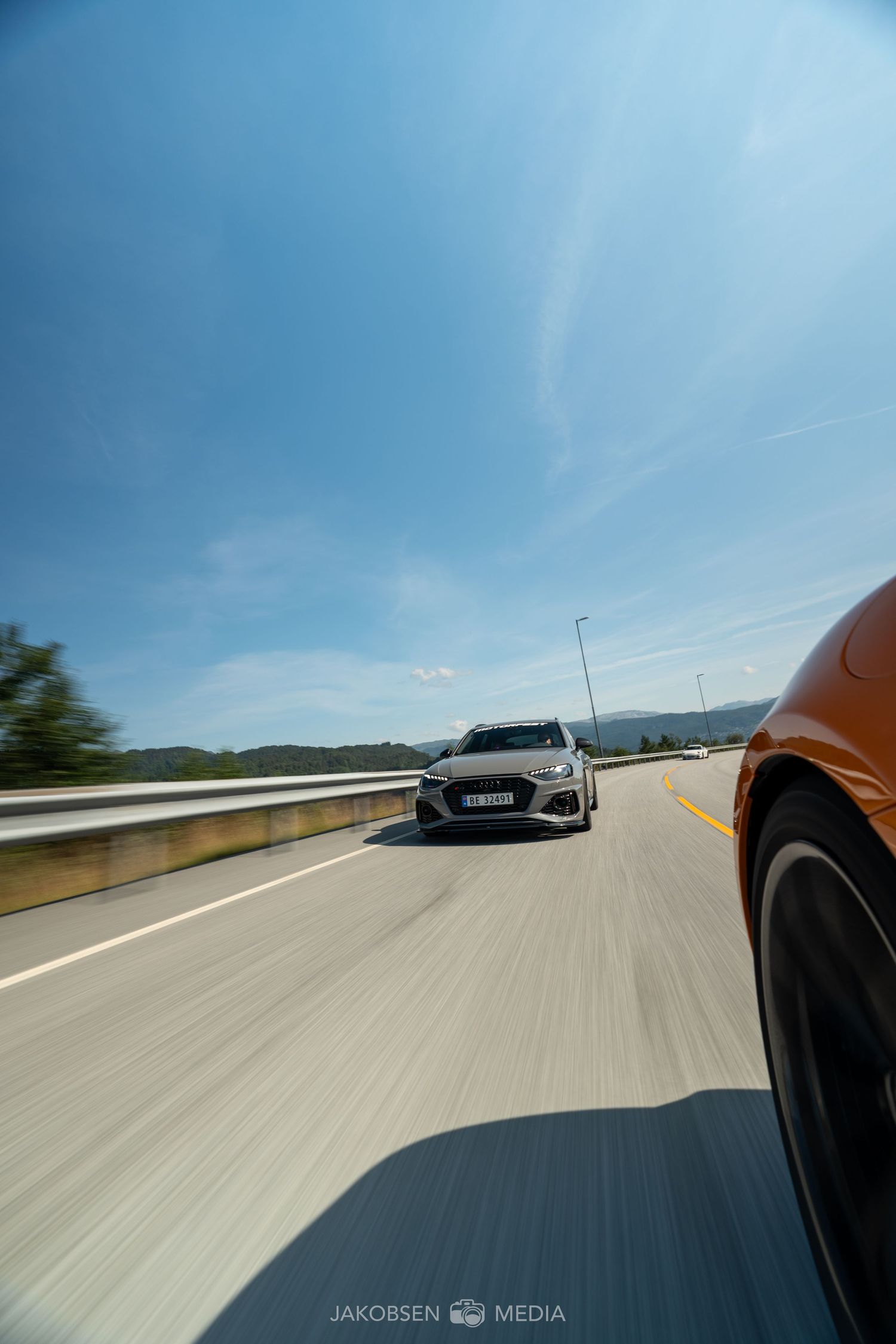 Point of view driving shot showing other sports cars on a scenic mountain highway.
