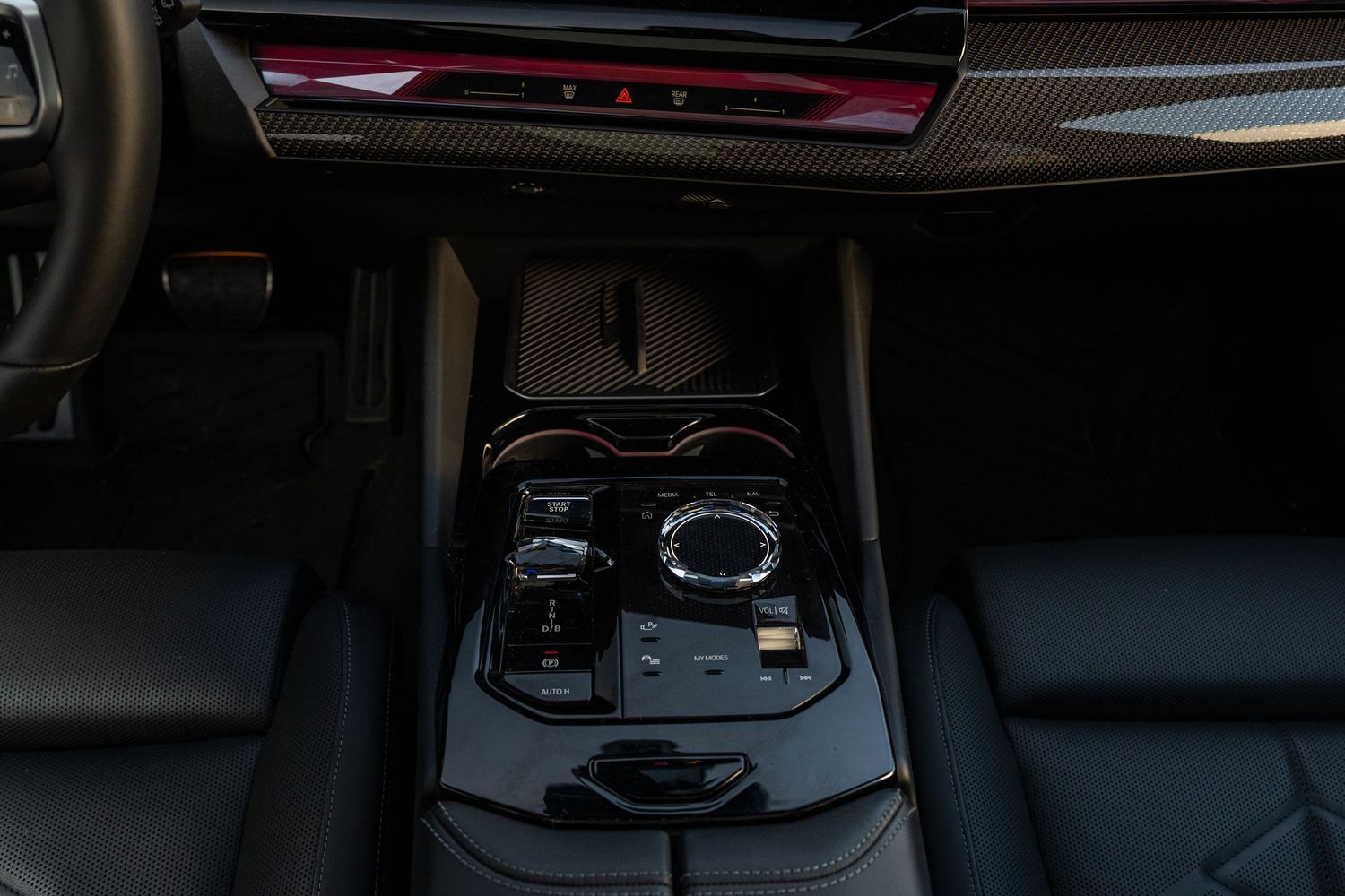 Center console of BMW showing gear selector and control knobs with carbon fiber trim.