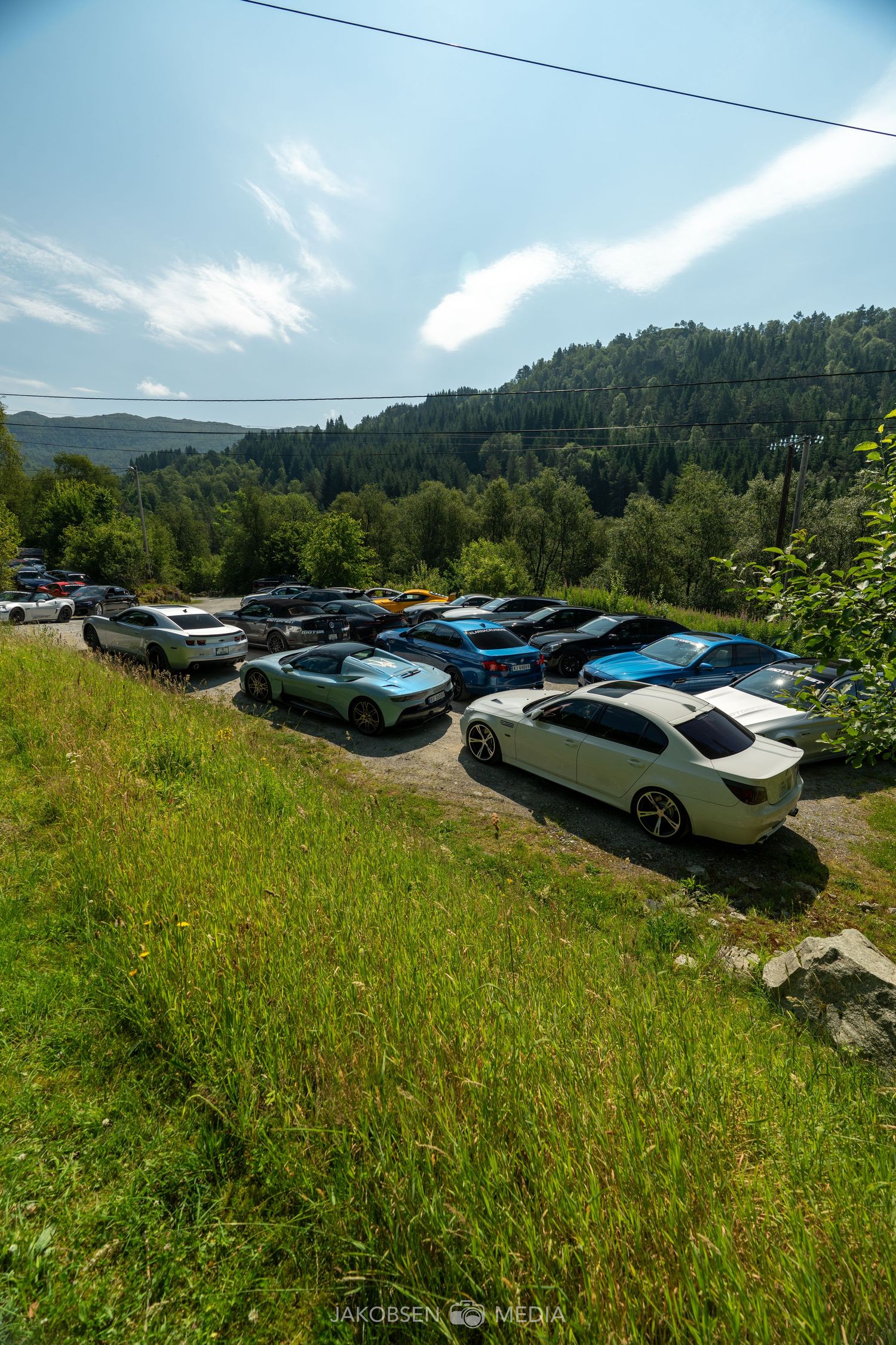 Panoramic view of luxury cars parked on hillside with mountain landscape in background.