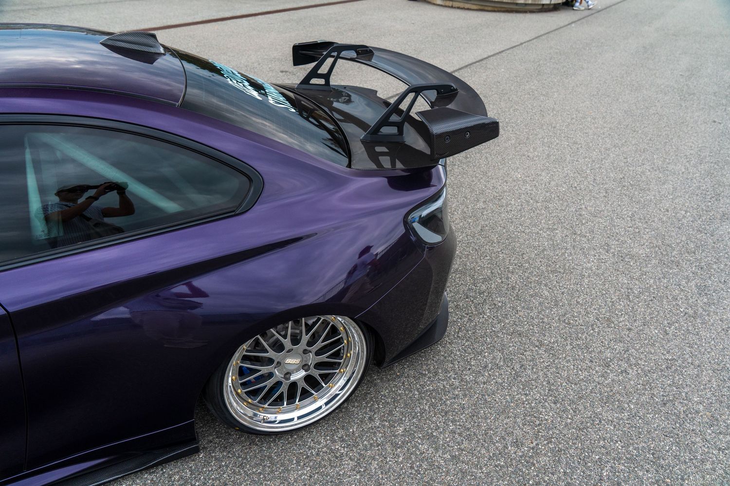 A modified purple BMW M4 showcasing its custom rear wing and aftermarket wheels.
