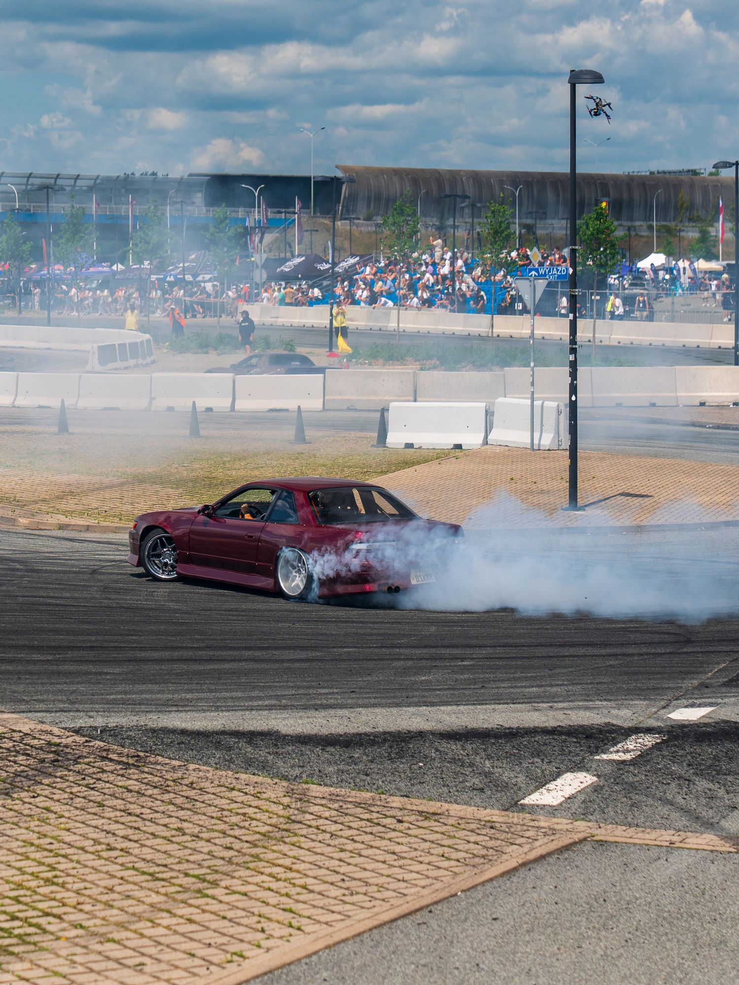 Red sports car performing drift with tire smoke at outdoor motorsport event.