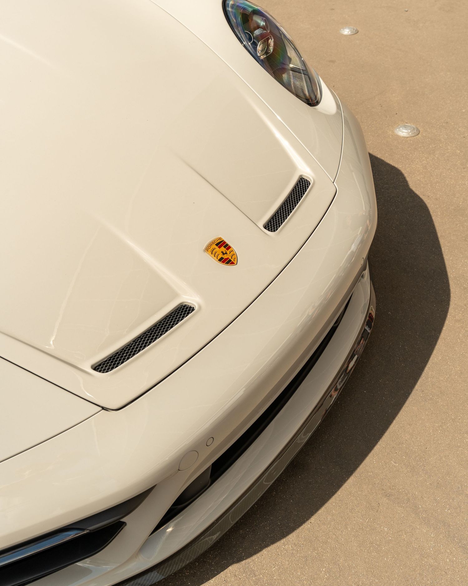 Front detail of a white Porsche showing the iconic hood badge and air intakes.