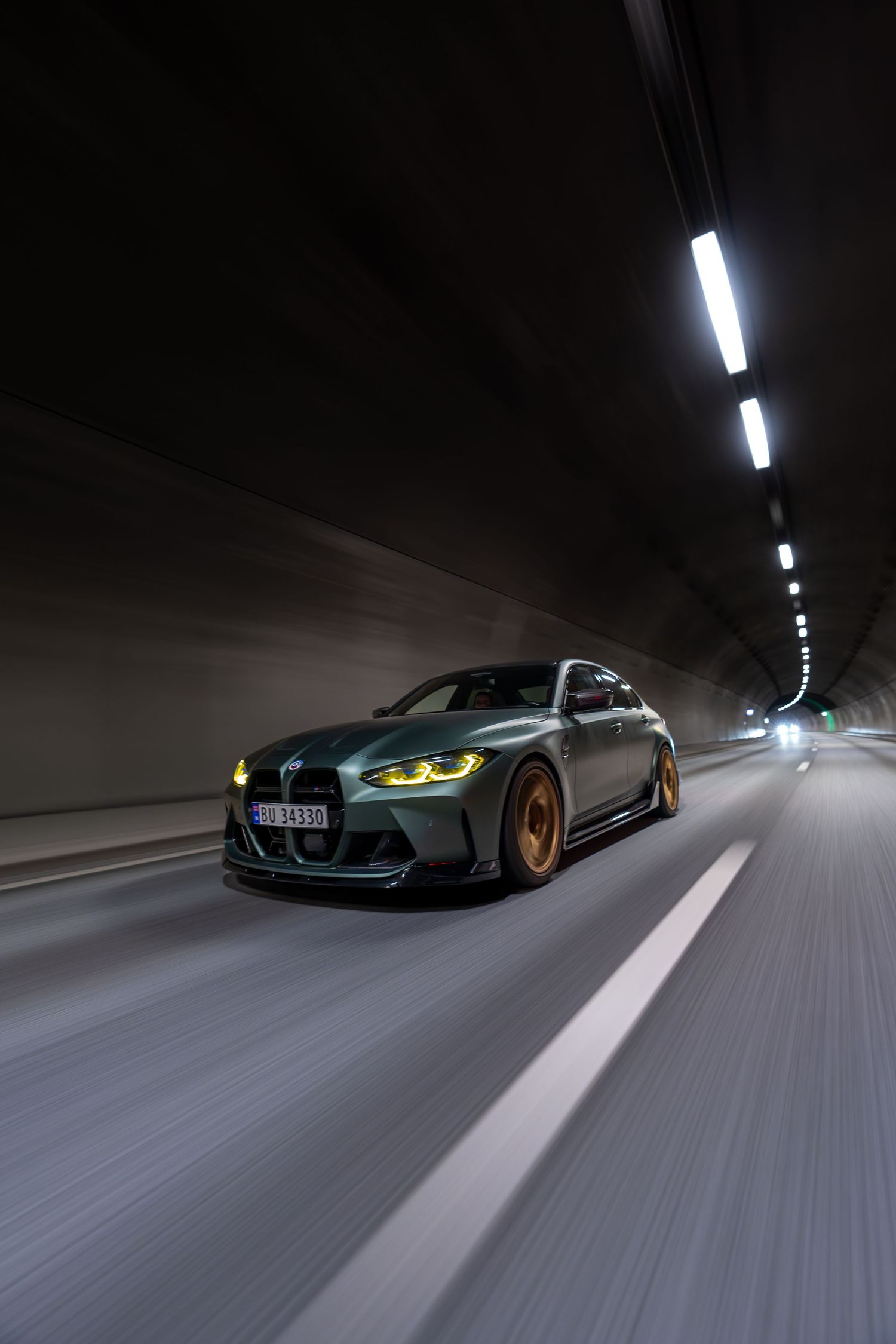 BMW M3 with glowing headlights driving through dark tunnel with motion blur.