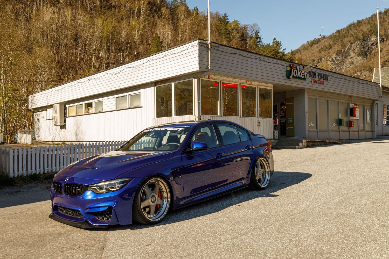 Modified blue BMW M3 parked in front of a white vintage diner building.