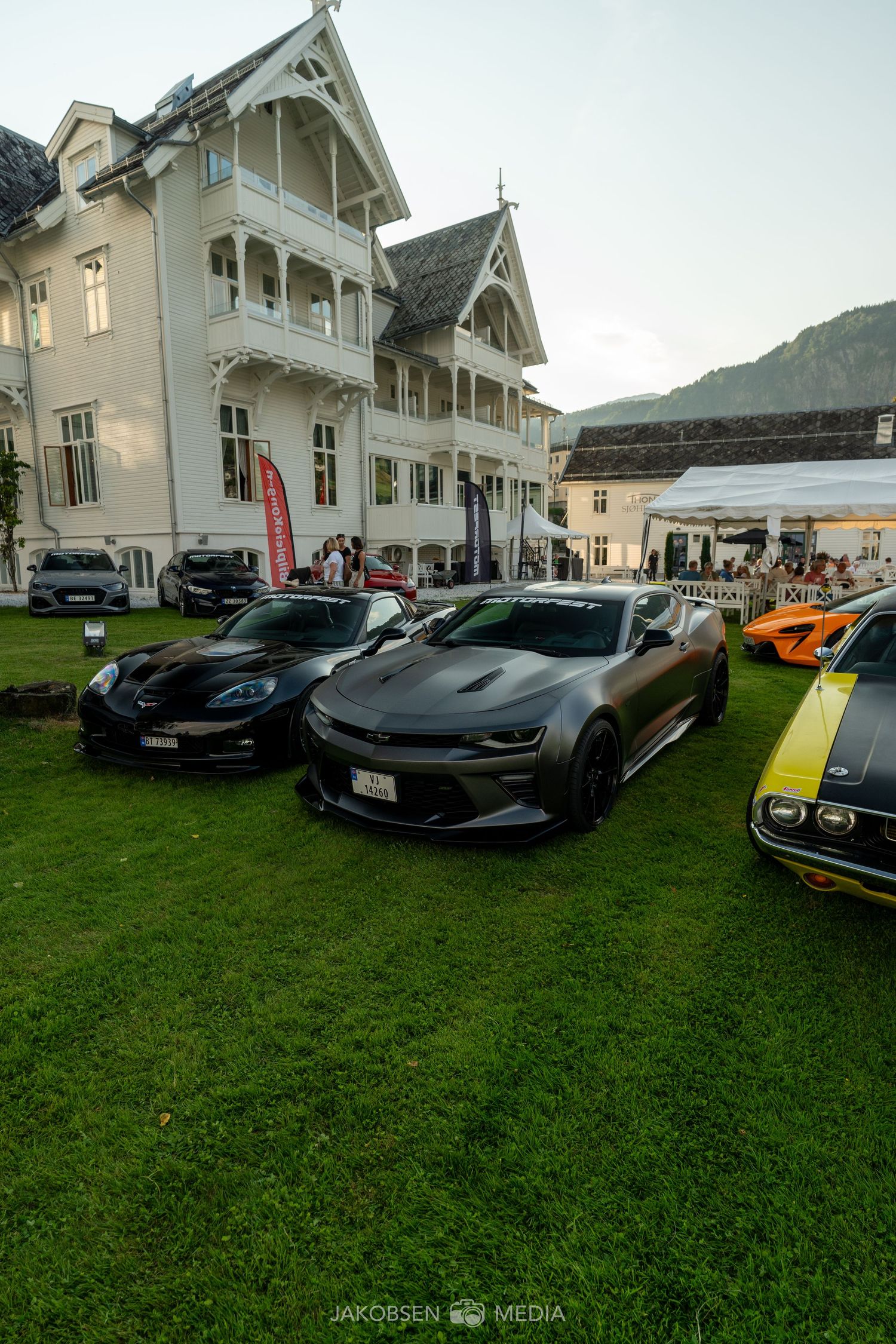 Luxury sports cars parked on grass with a white Victorian-style building in the background.
